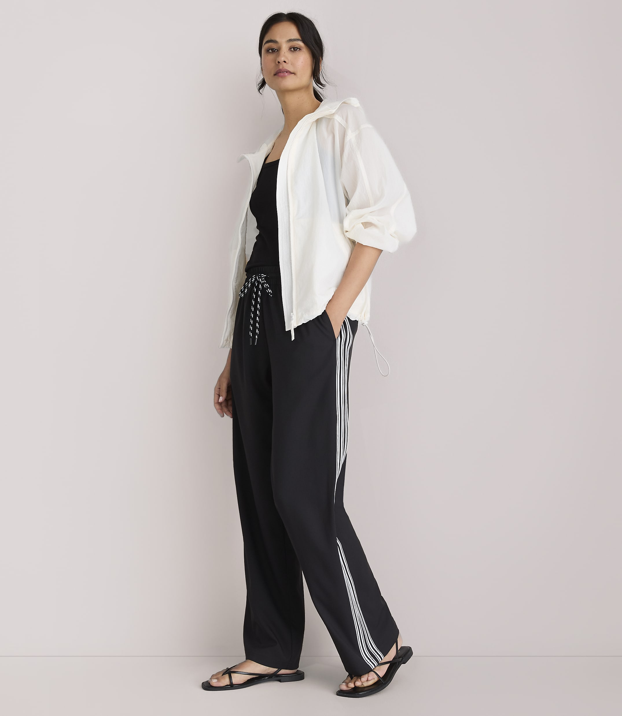 A woman in a white jacket and black athletic pants stands against a plain white background.