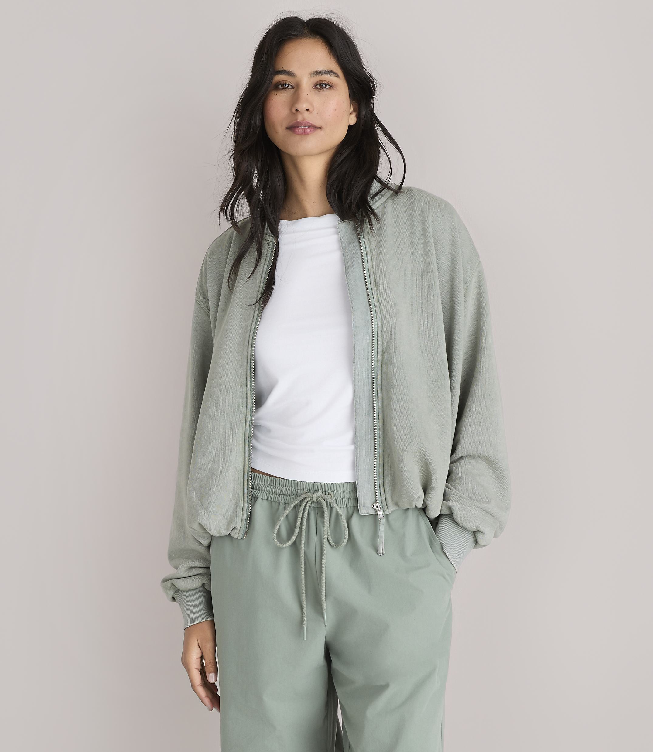 A woman in a light green bomber jacket and matching pants stands against a plain white background.