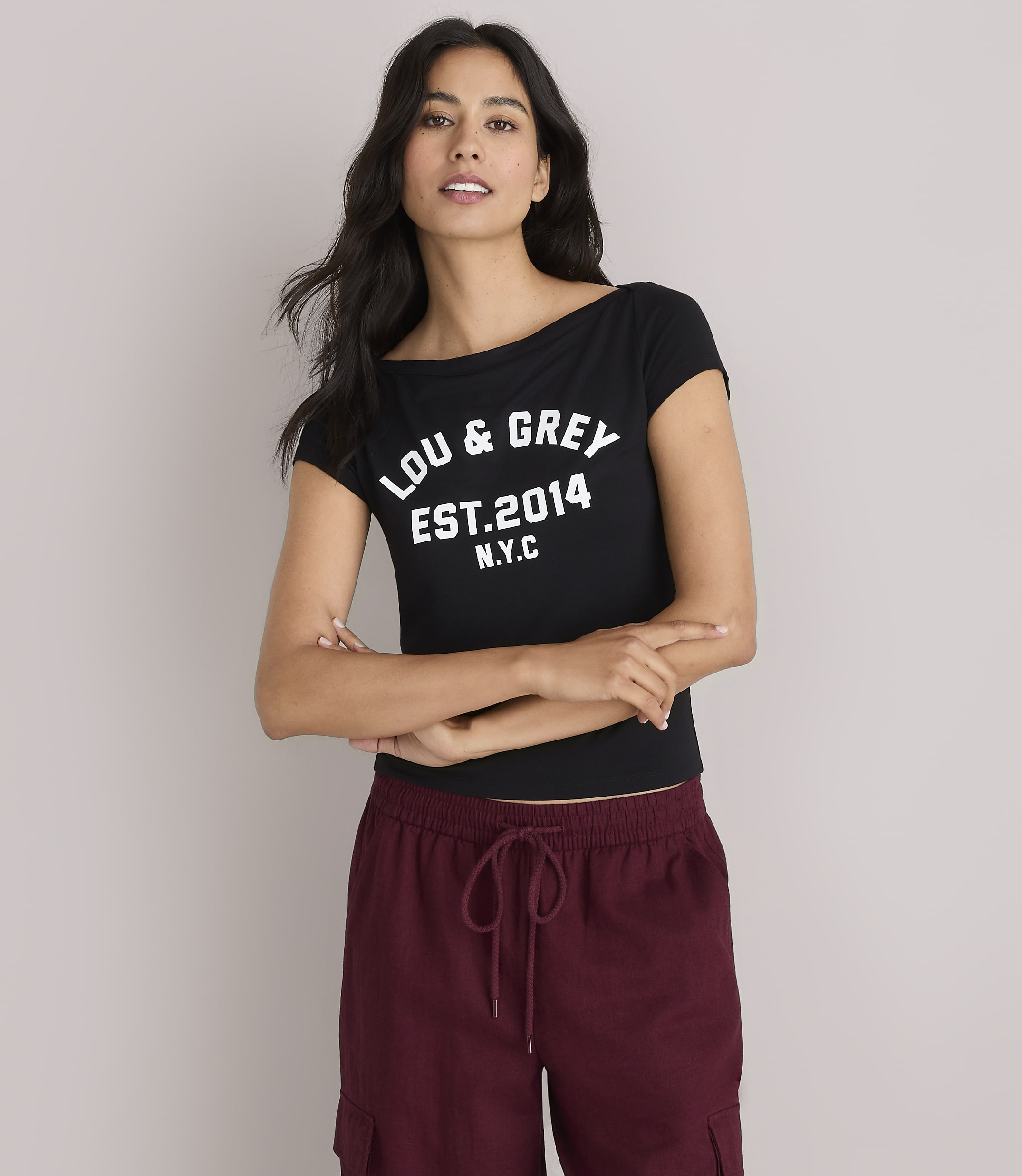 A woman in a black "LOU & GREY EST. 2014 N.Y.C." t-shirt and maroon cargo pants stands against a plain white background.