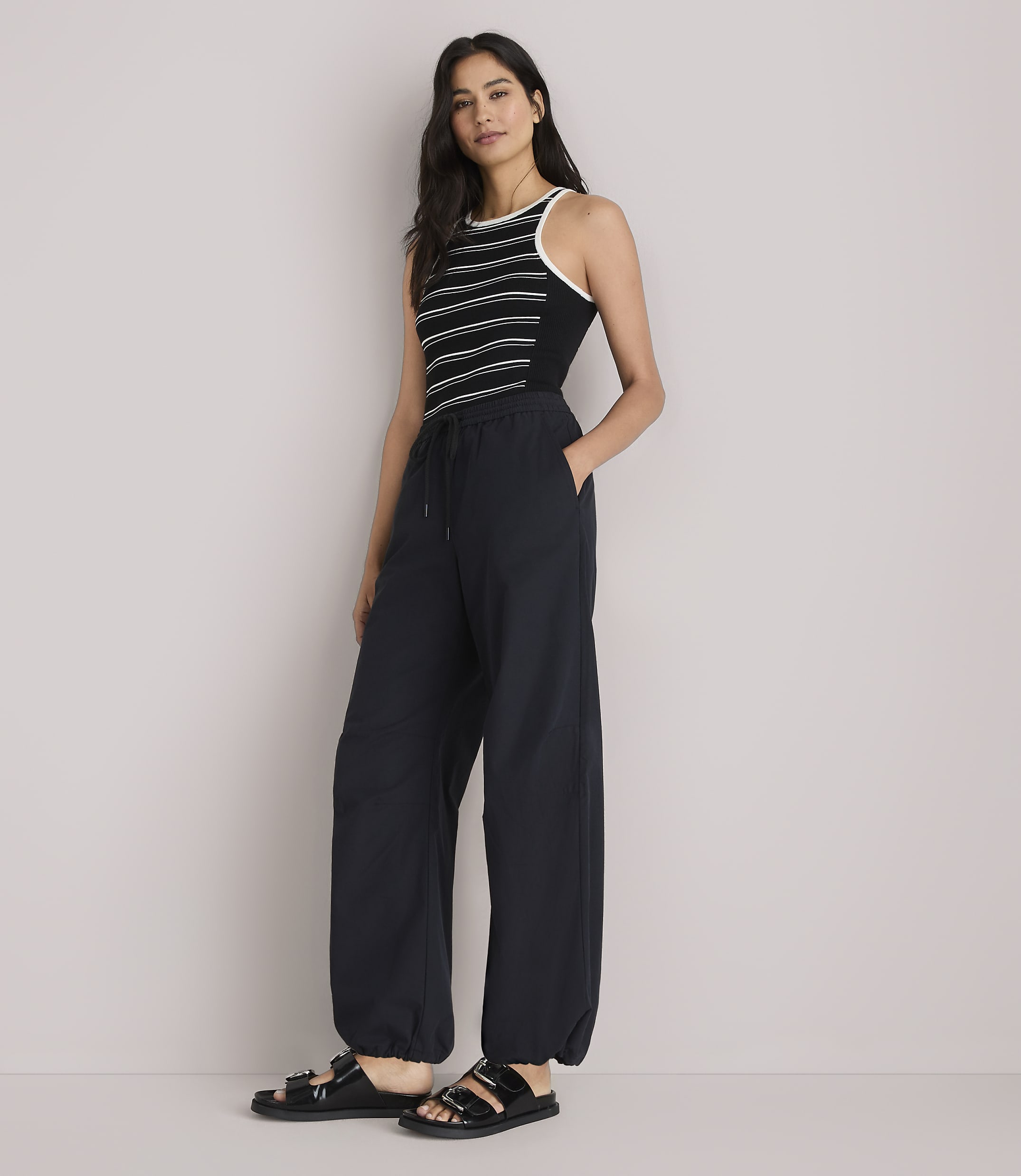 A woman in a striped tank top and baggy pants stands against a plain white background.