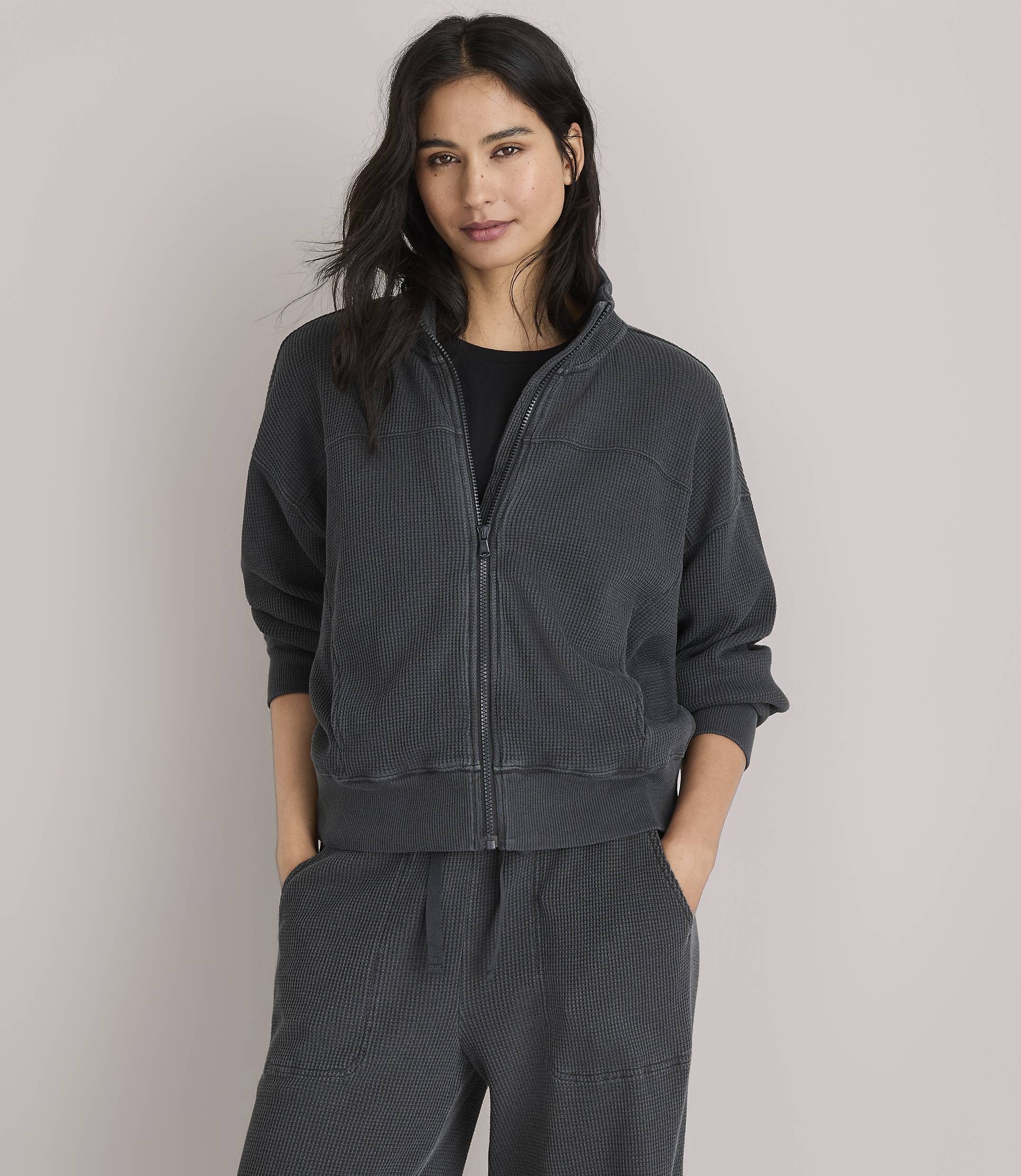 A woman in a dark grey waffle-knit jacket and pants poses against a plain white background.