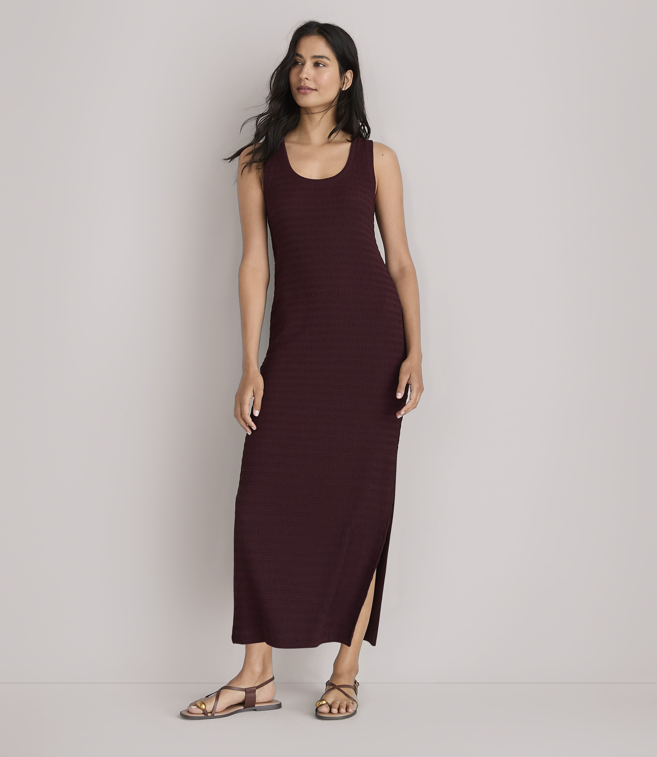 A woman in a maroon maxi dress stands against a plain white background.