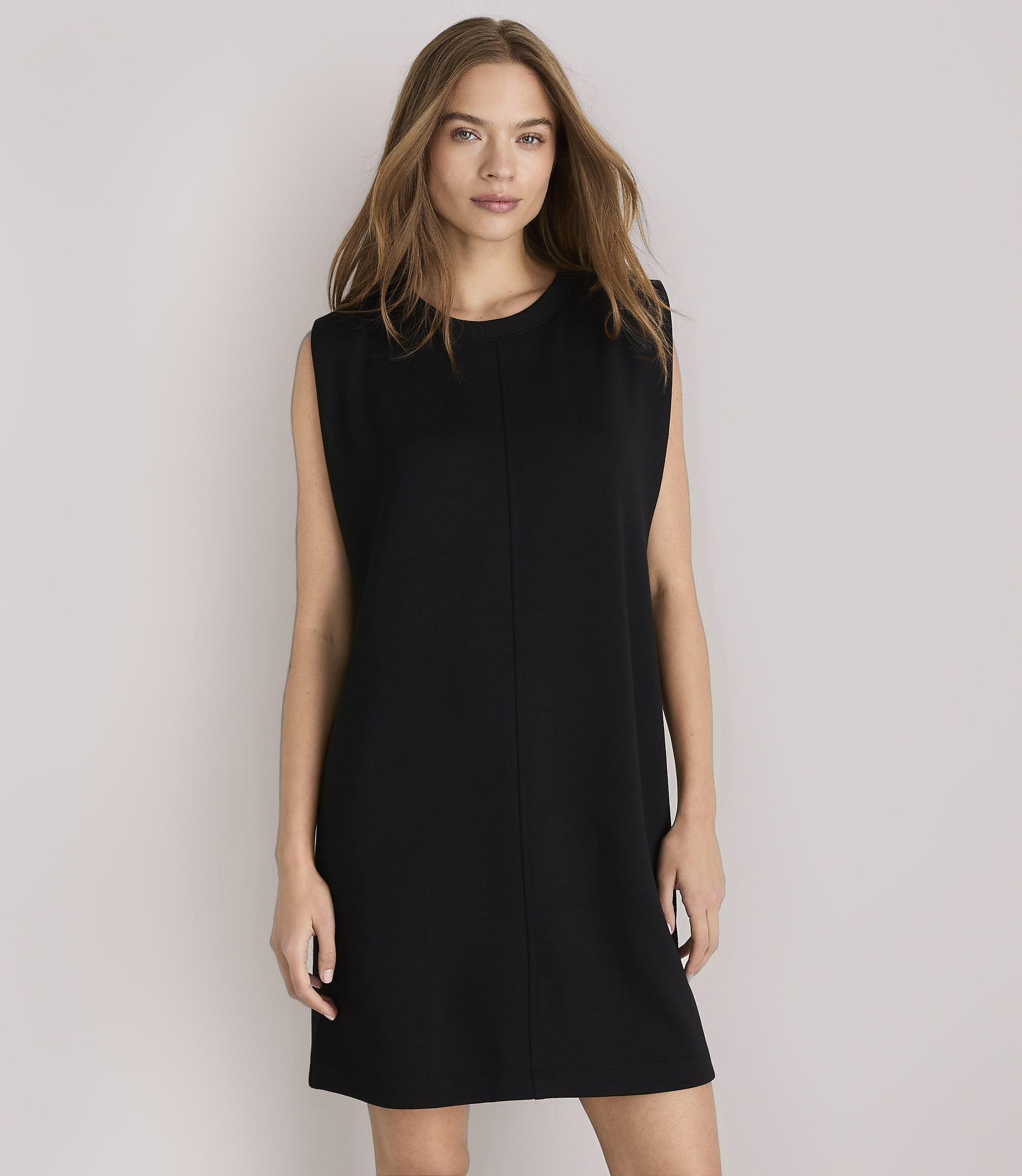 A woman in a black shift dress stands against a plain white background.