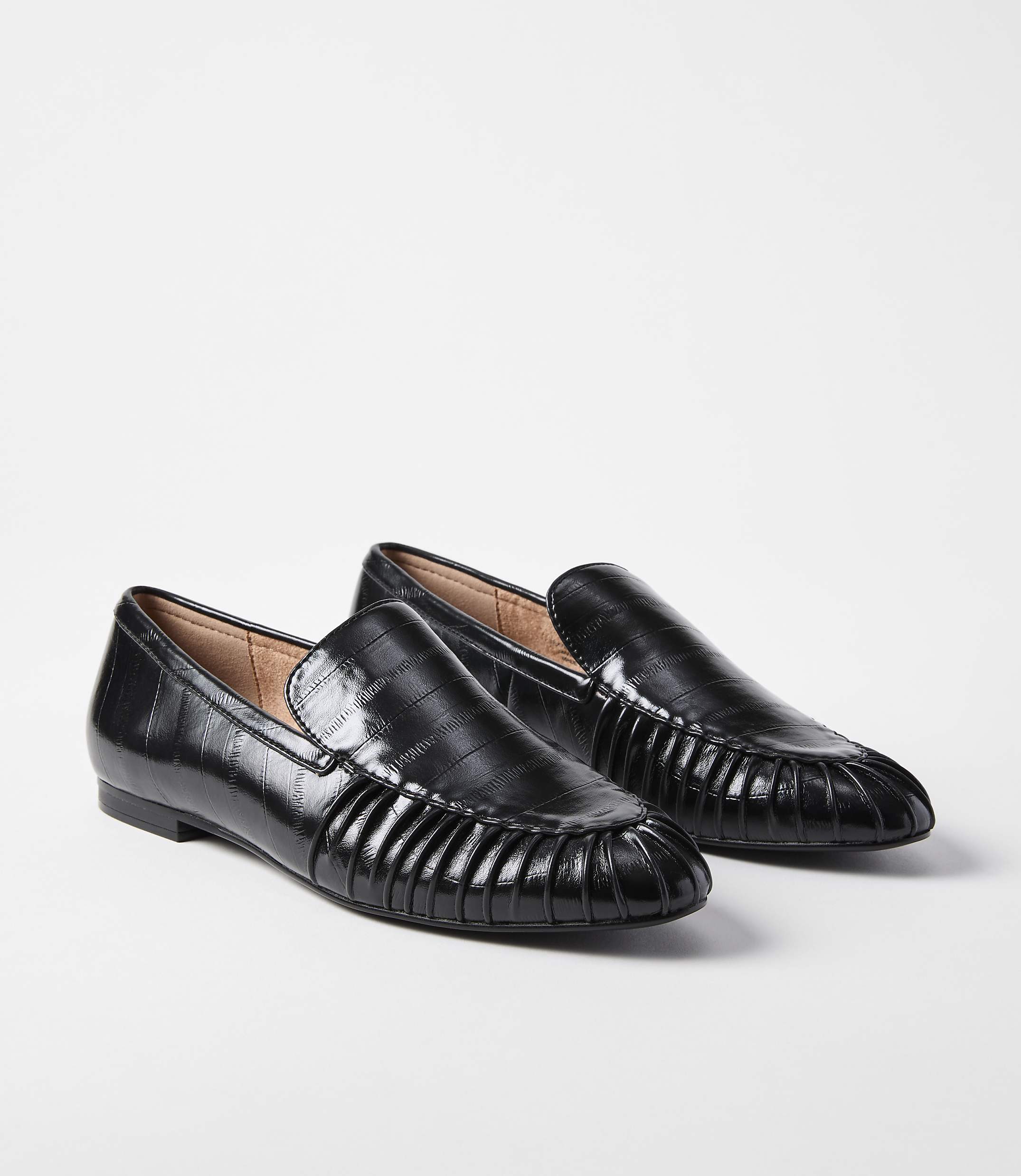 A pair of black, croc-embossed loafers with pleated detailing on the vamp rest on a plain white background.