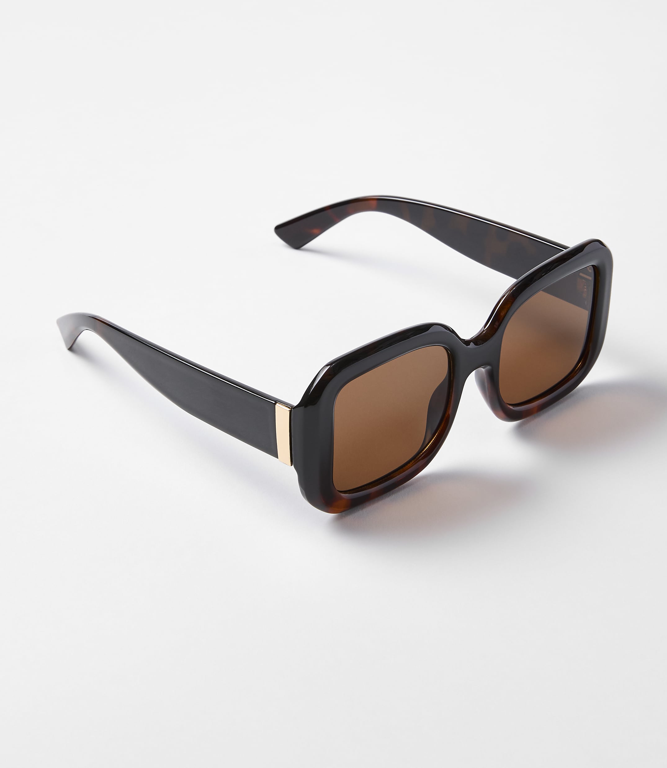 A pair of tortoiseshell sunglasses with brown lenses rests on a plain white background.