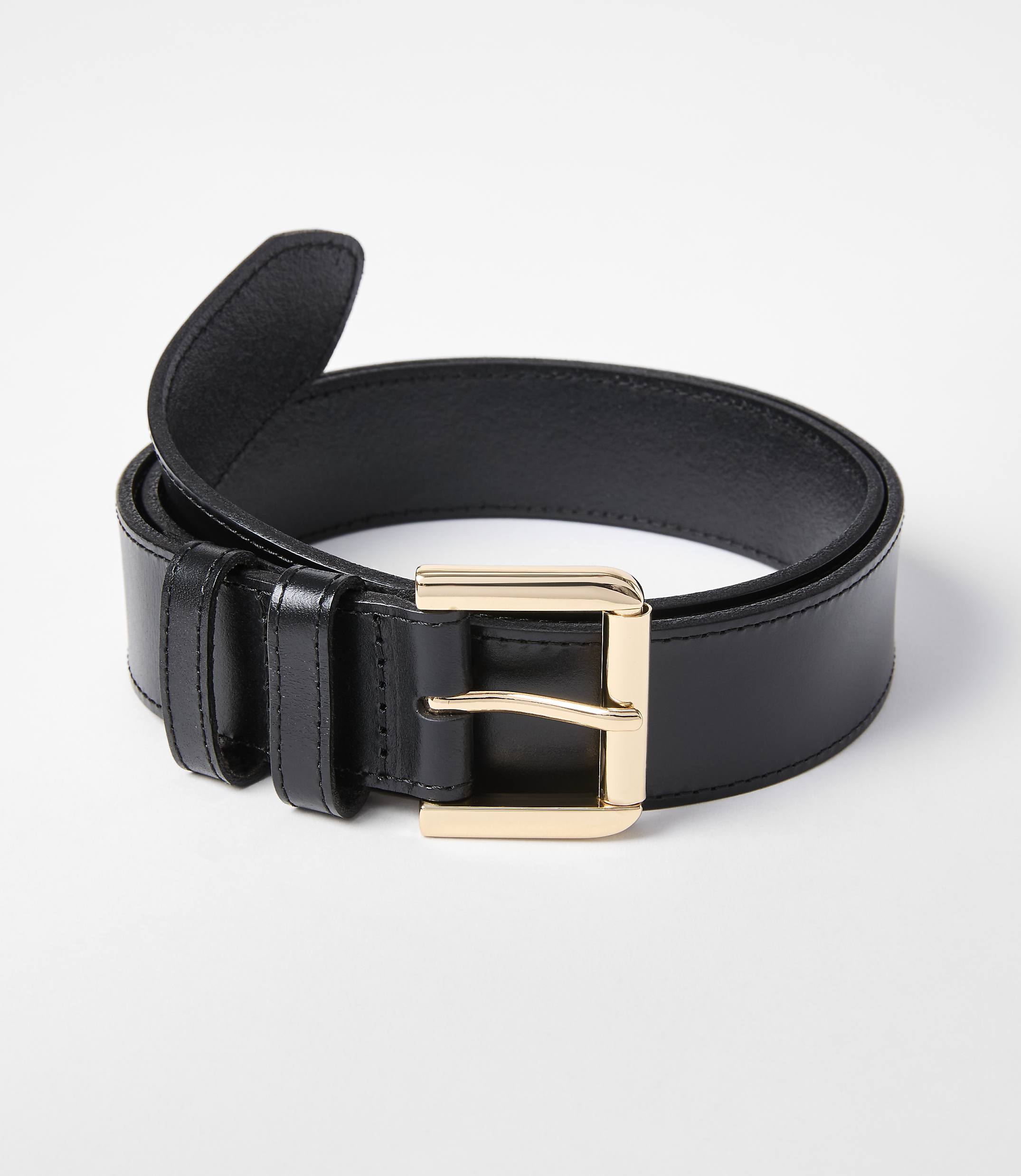 A black leather belt with a gold buckle rests on a white background.