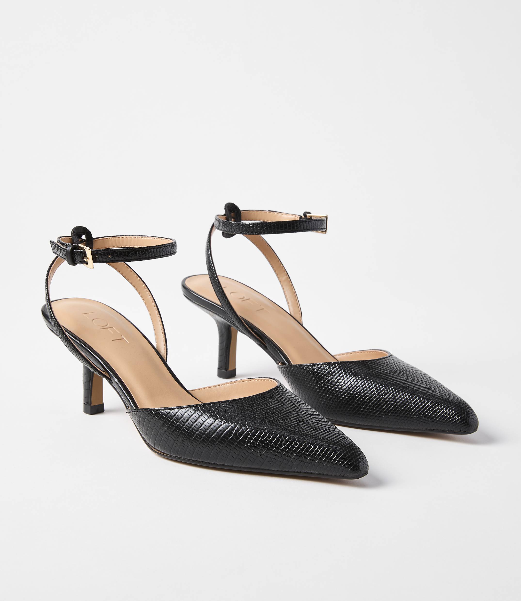 A pair of black, textured leather slingback heels with ankle straps are displayed against a plain white background.
