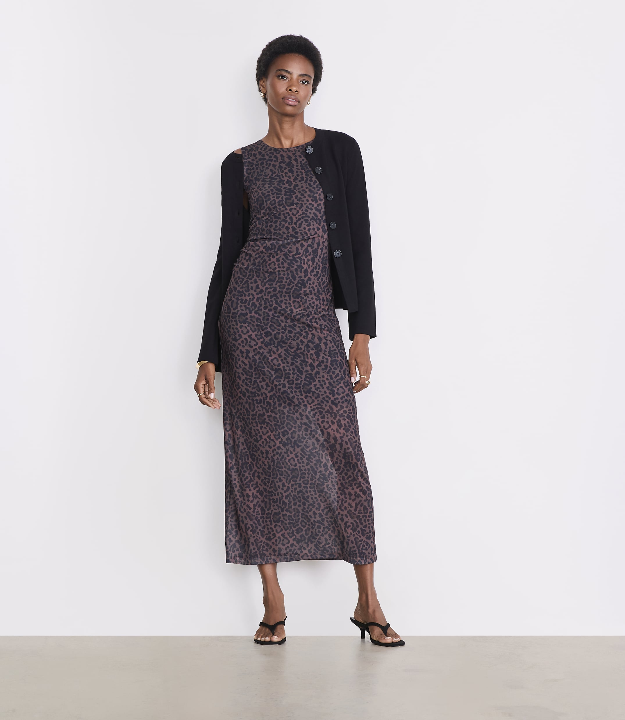 A woman in a leopard print dress and black cardigan stands against a plain white background.