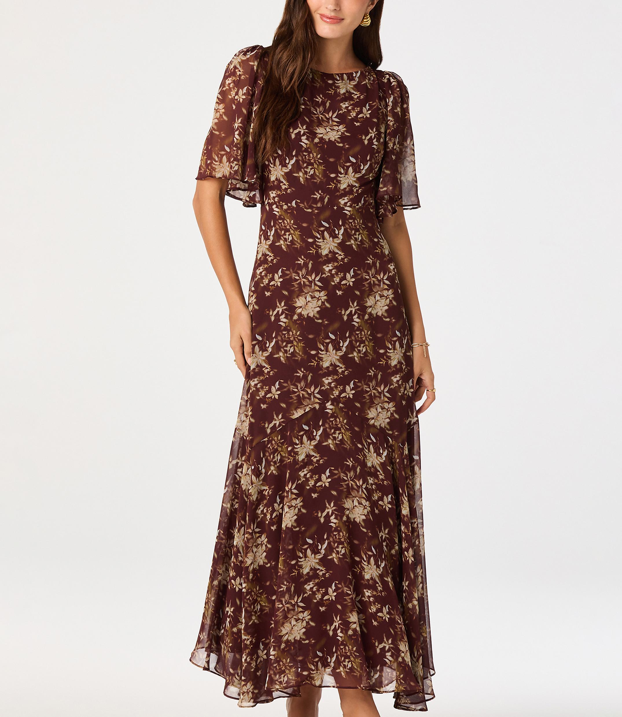 A woman in a floral dress stands against a plain white background.