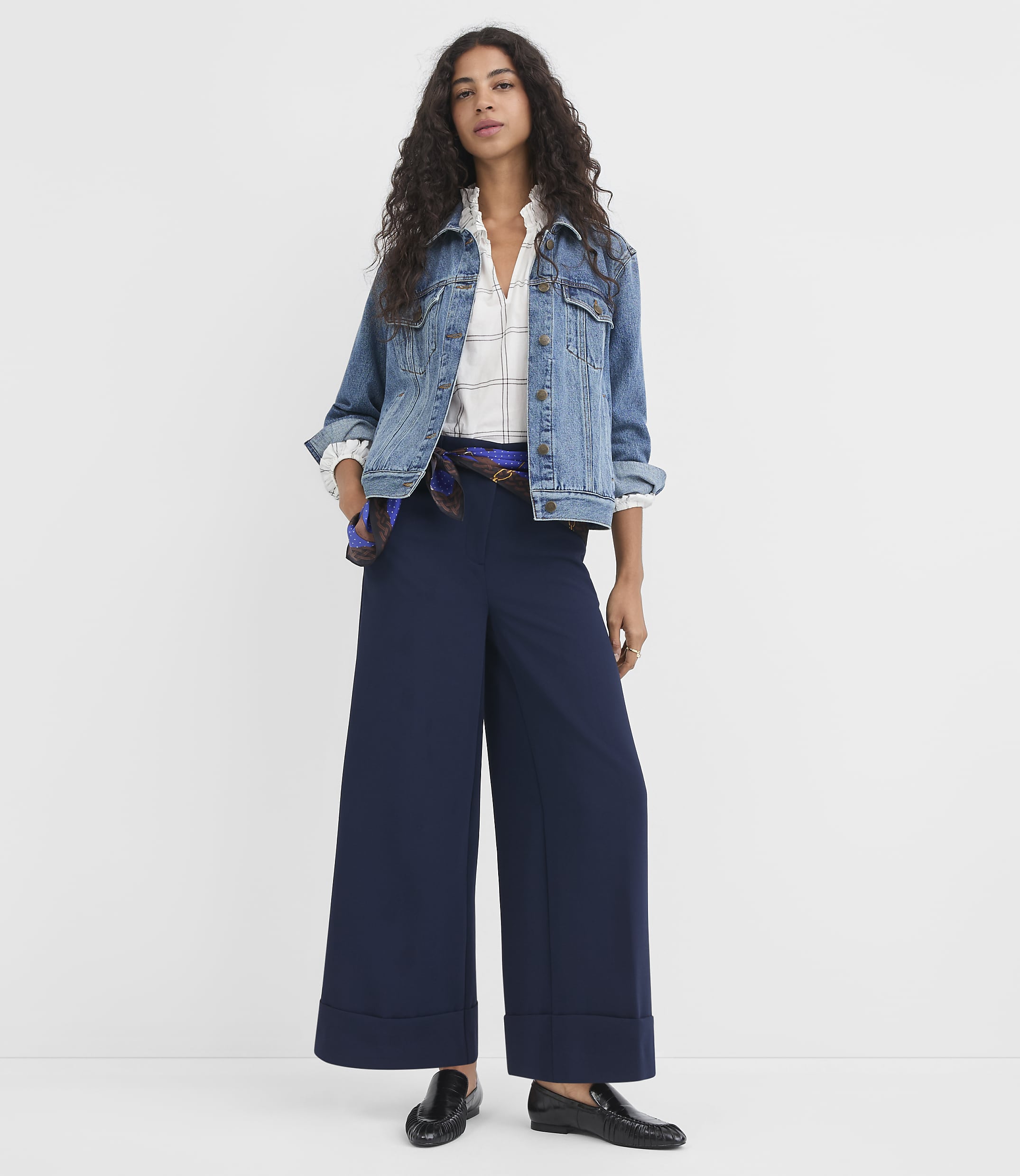 A woman in a denim jacket and wide-leg navy pants stands against a plain white background.