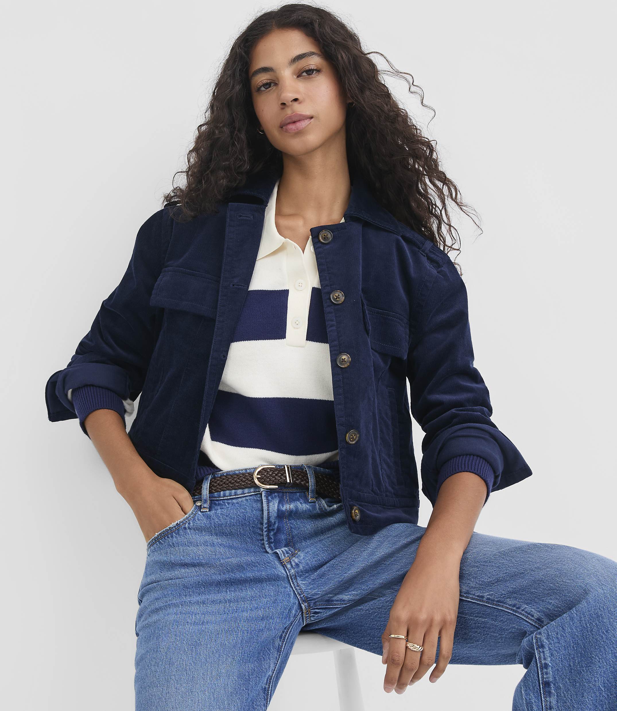 A woman in a navy corduroy jacket and blue jeans poses against a plain white background.