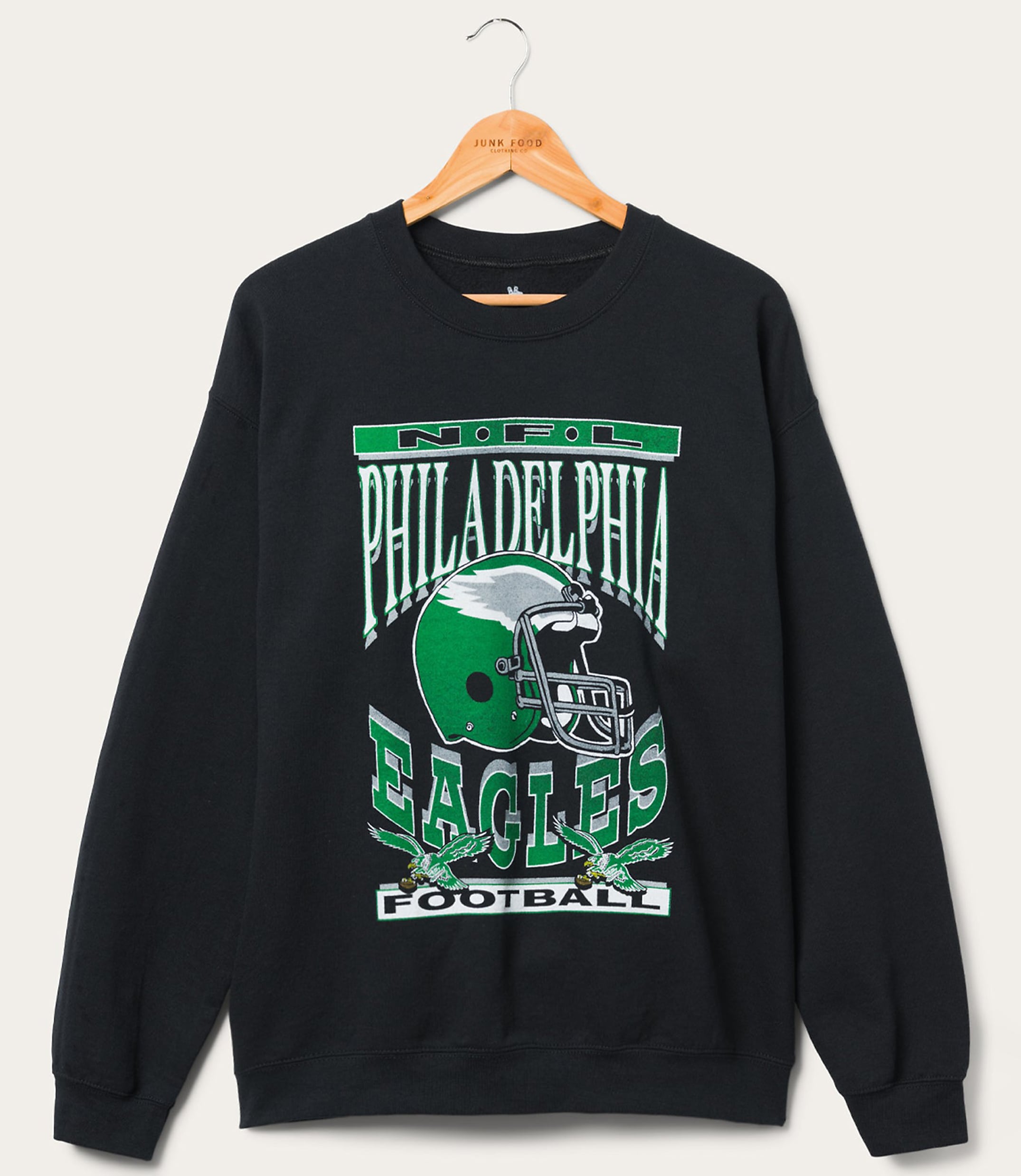 A black Philadelphia Eagles sweatshirt with a graphic of a helmet and eagles hangs on a wooden hanger against a plain white background.