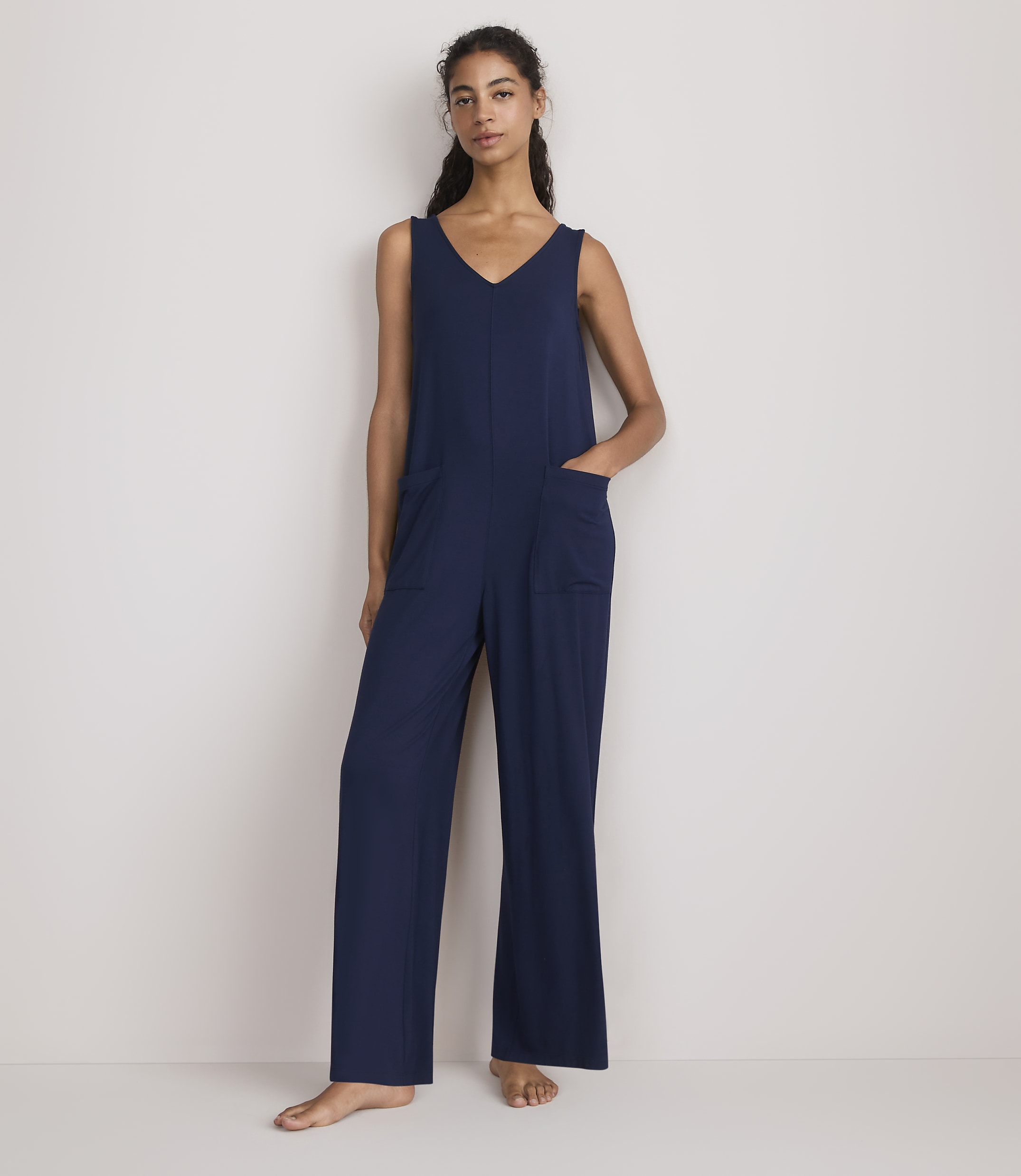 A woman in a navy blue jumpsuit stands against a plain white background.