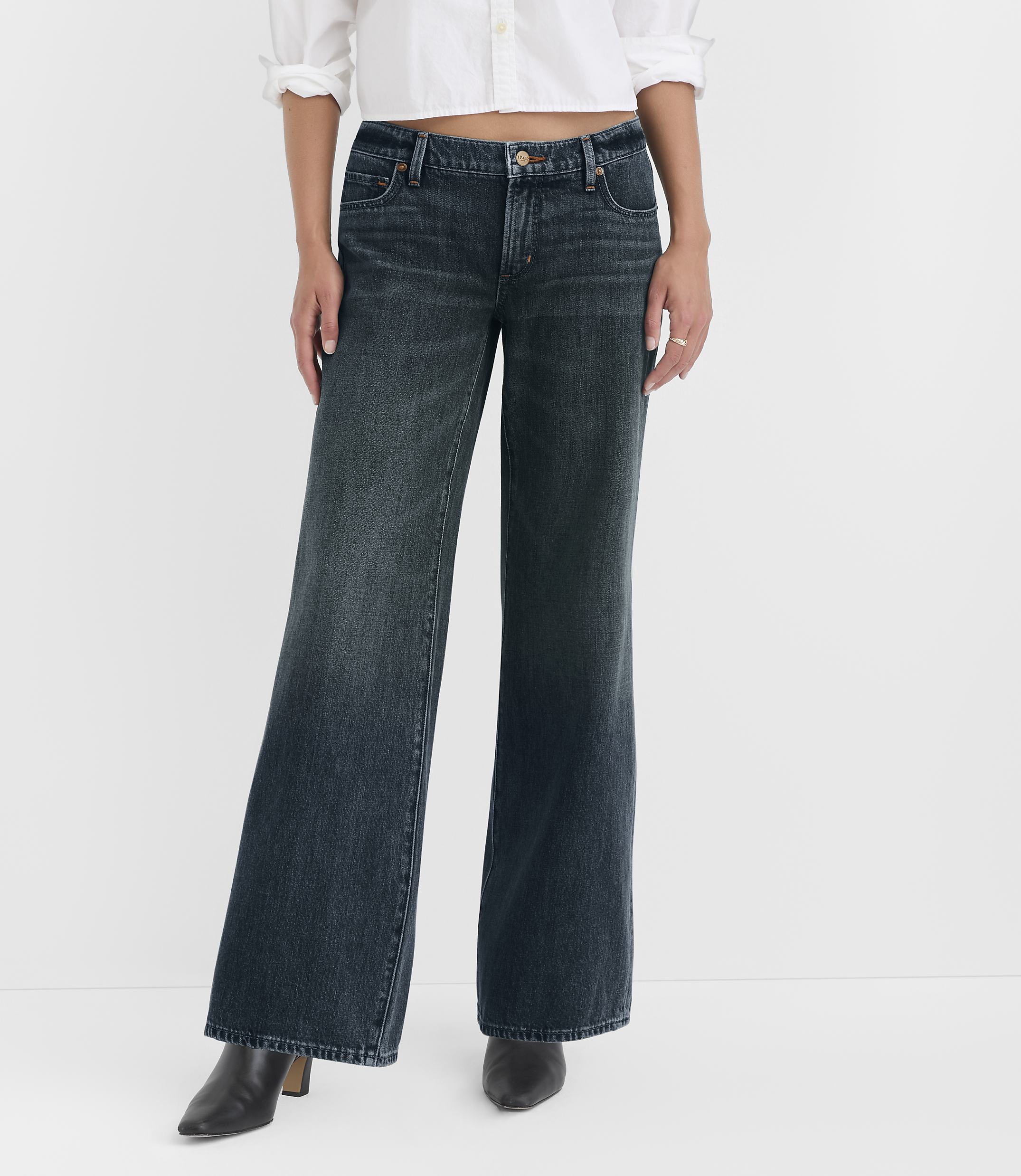 A person wearing wide-leg dark wash jeans and black heeled boots stands against a plain white background.