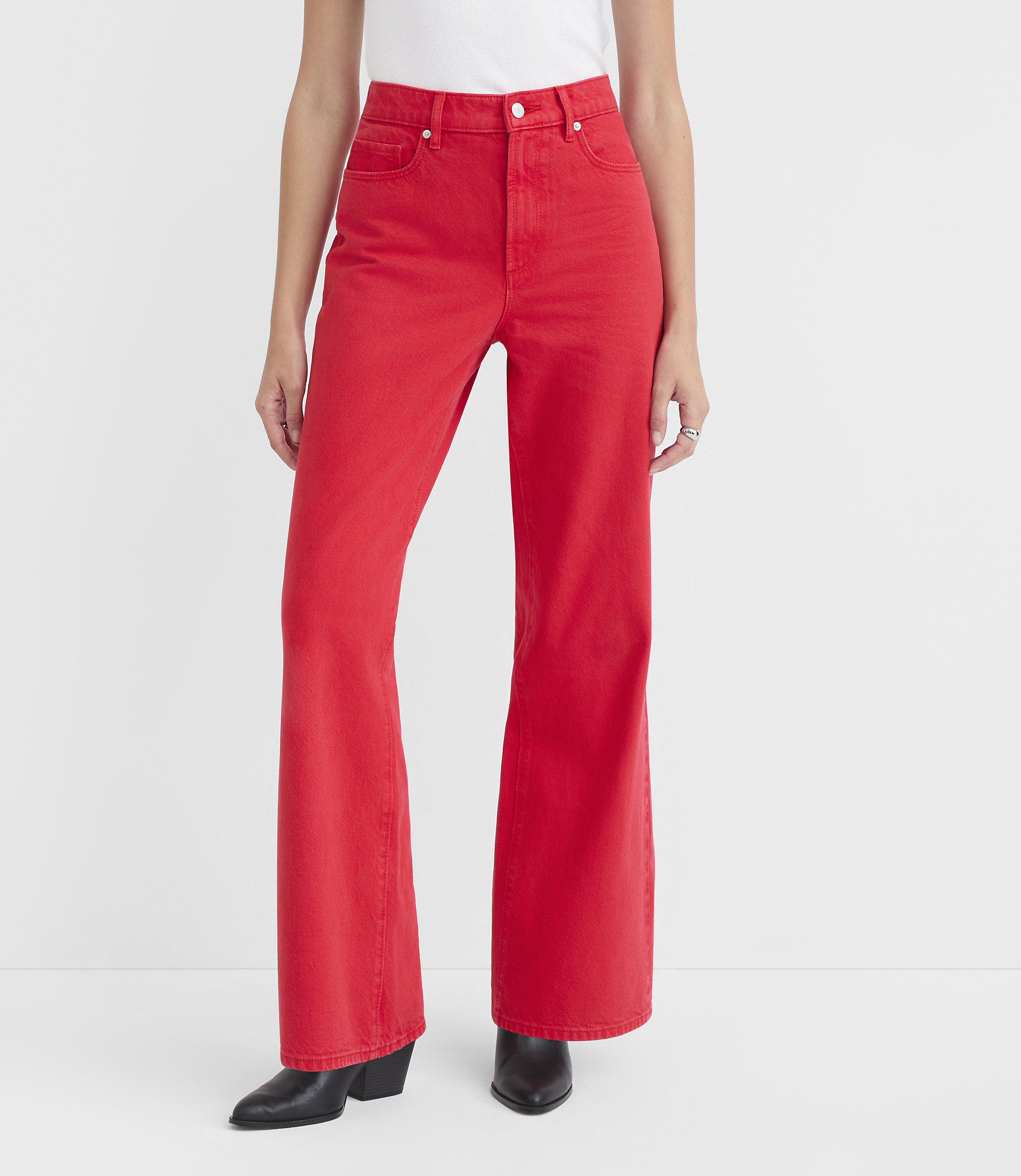 A person stands in the foreground wearing bright red flared jeans and black boots against a plain white background.