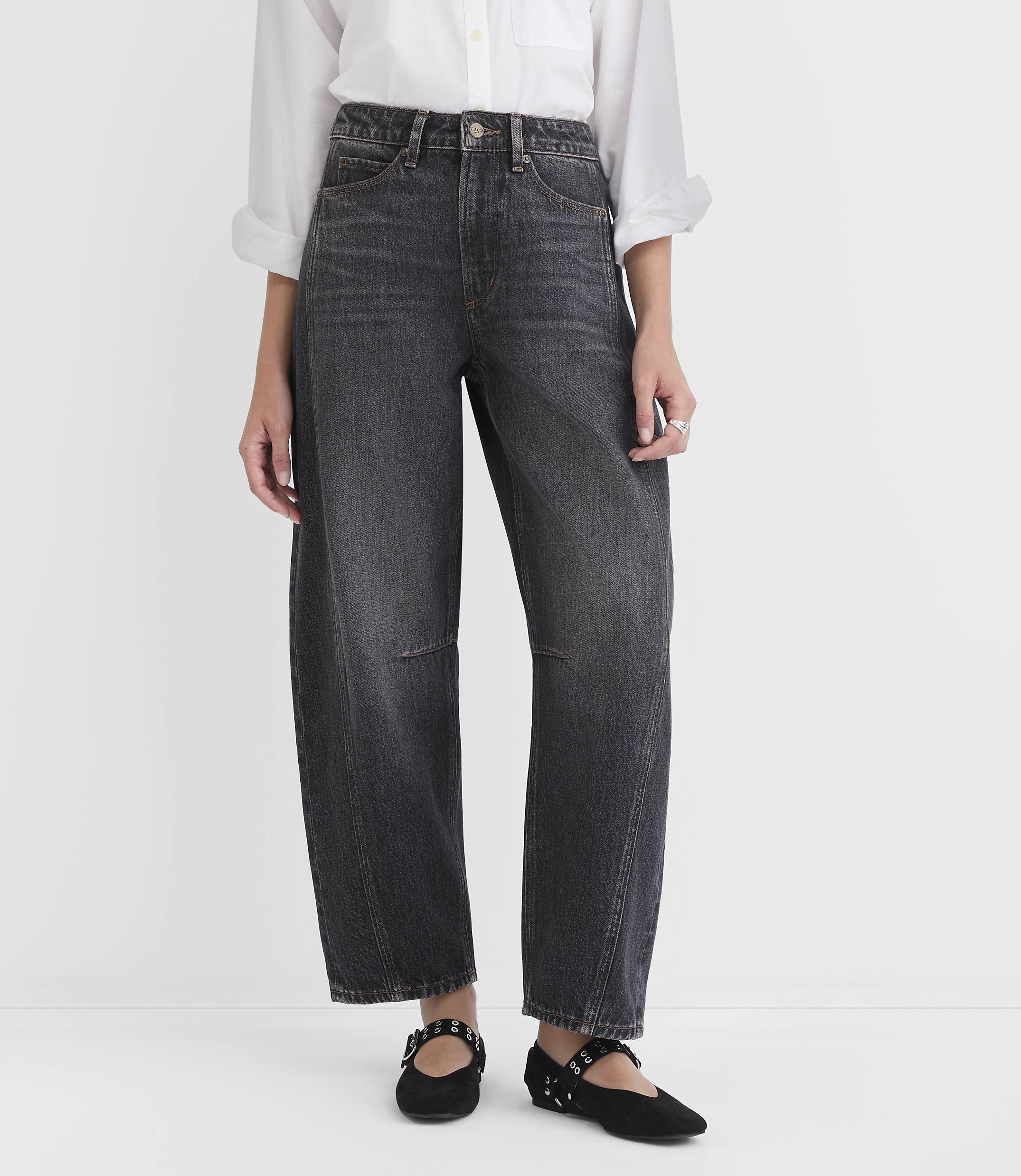 A person wearing dark wash, wide-leg jeans and black studded flats stands against a plain white background.