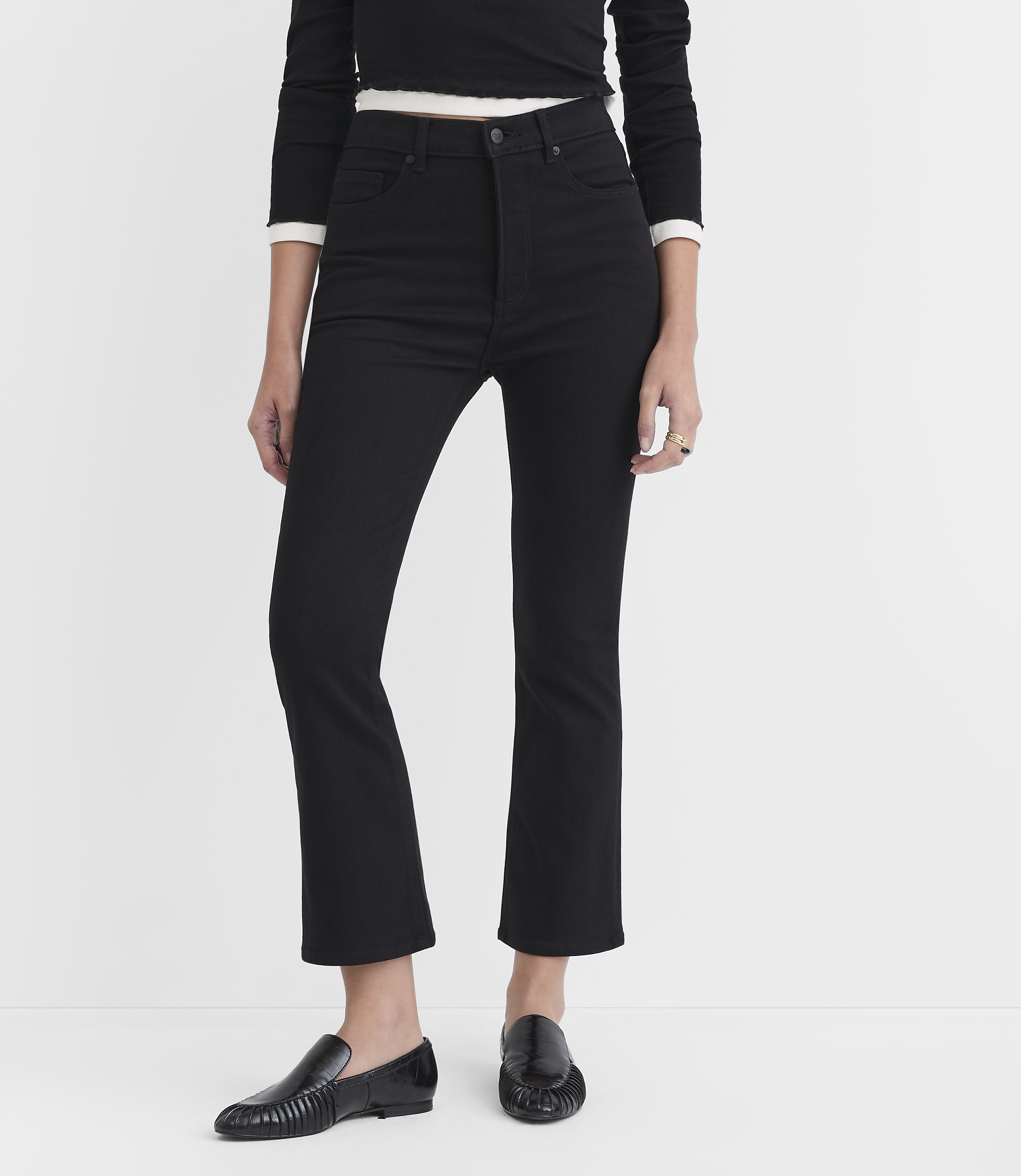 A person wearing black jeans and loafers stands against a plain white background.