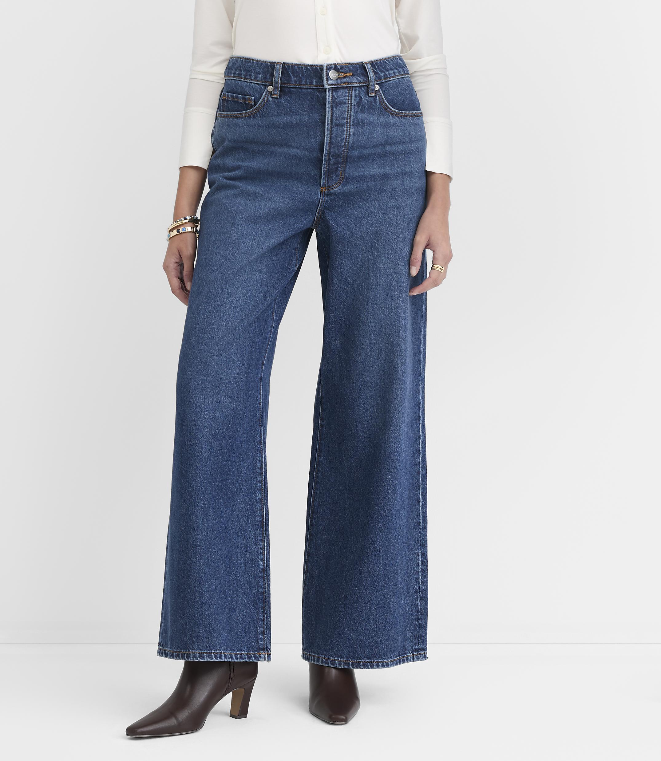A person in wide-leg jeans and a white shirt stands against a plain white background.