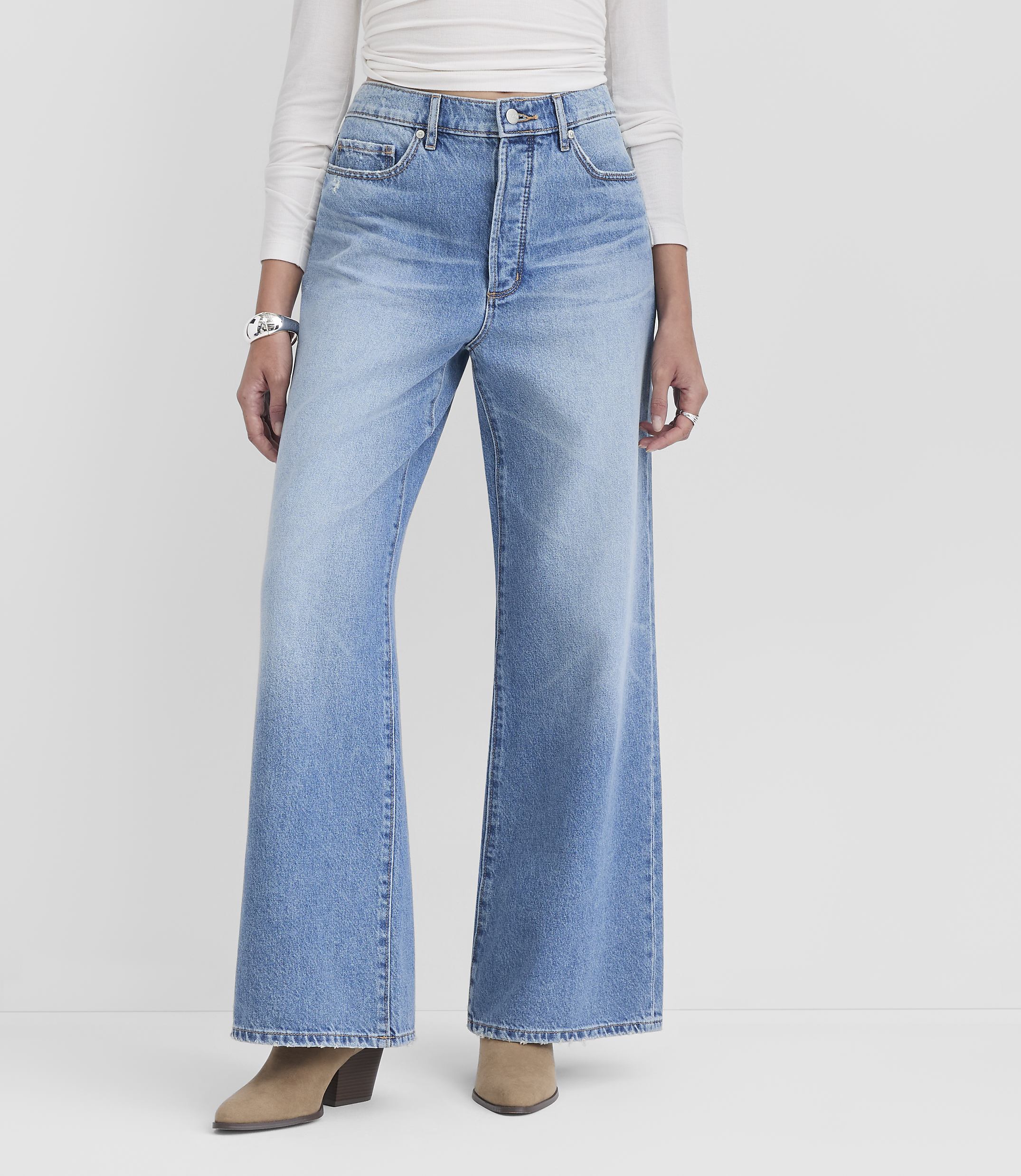 A person models light-wash wide-leg jeans and tan heeled boots against a plain white background.