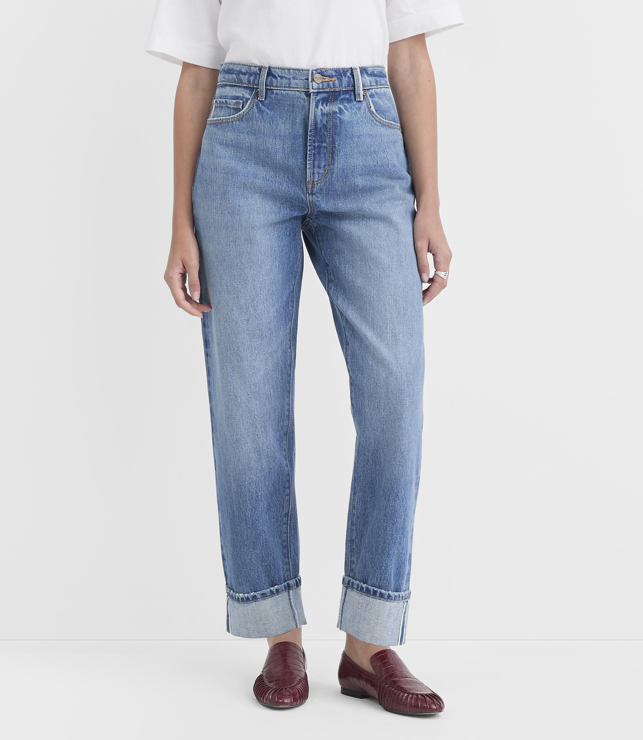 A person stands in light blue cuffed jeans and burgundy loafers against a plain white background.