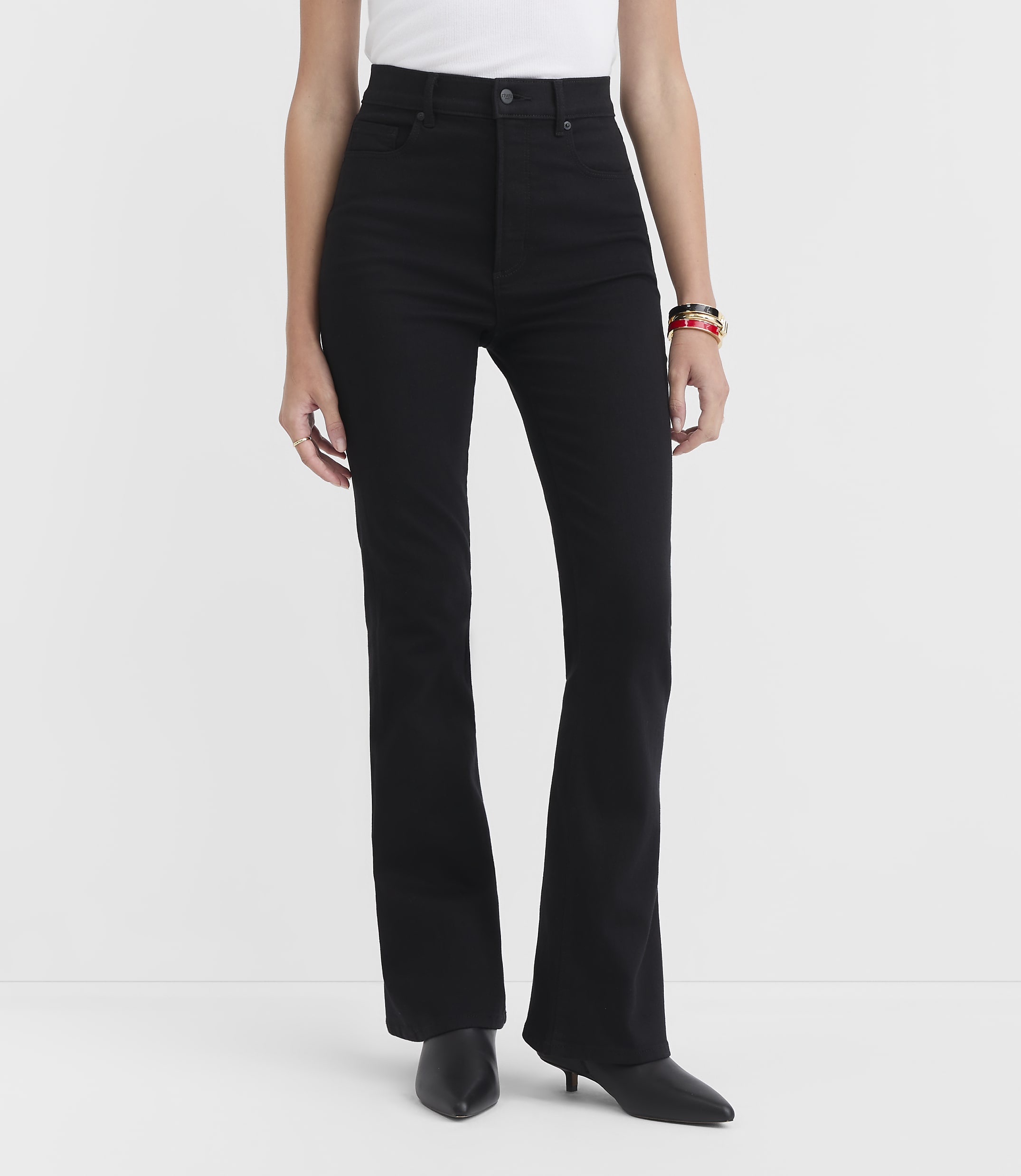 A person stands in black flare jeans and black heels against a plain white background.