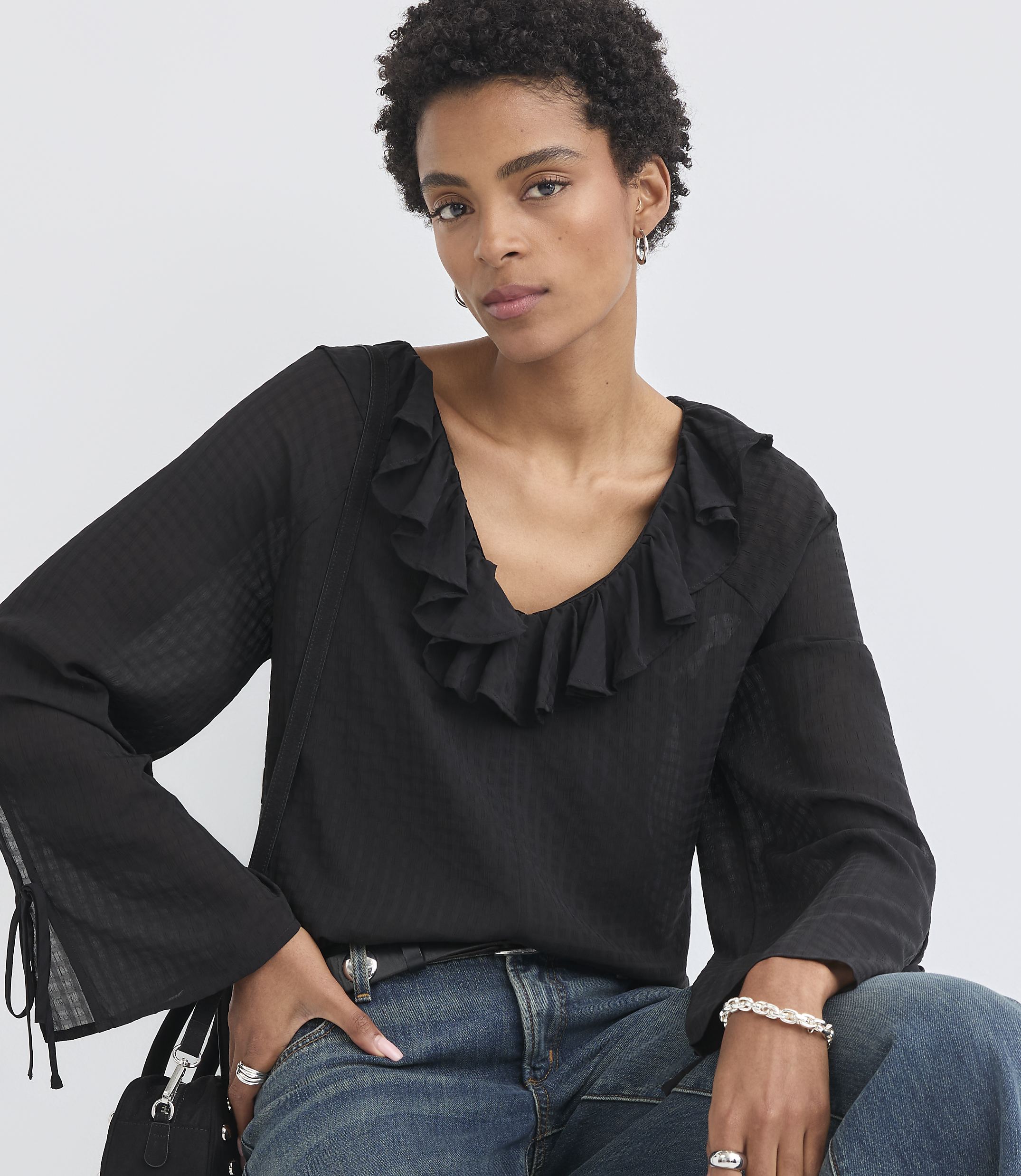 A woman with short, dark hair and a ruffled black blouse poses against a plain white background.