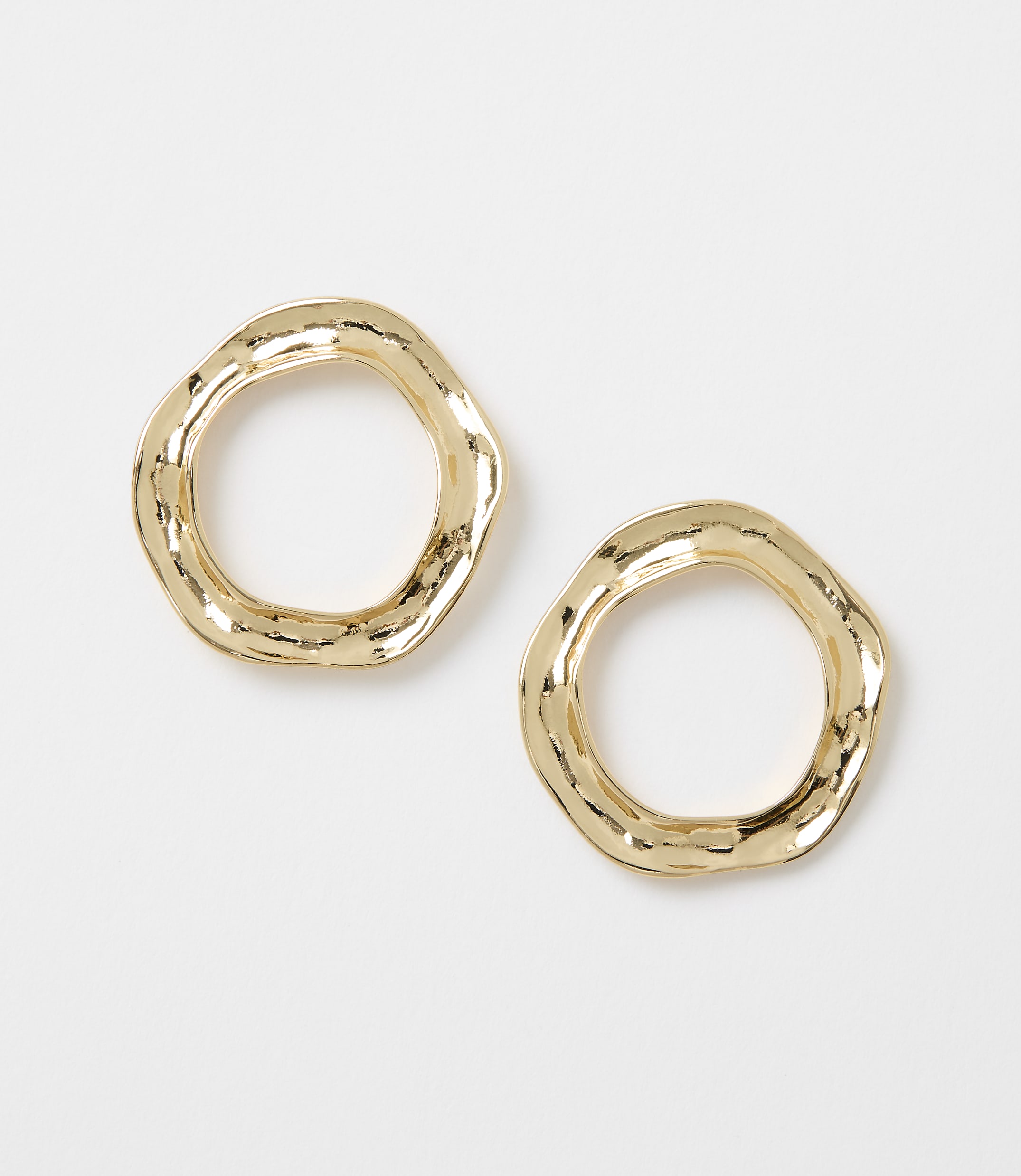 Two irregular, hammered gold hoop earrings rest on a plain white background.