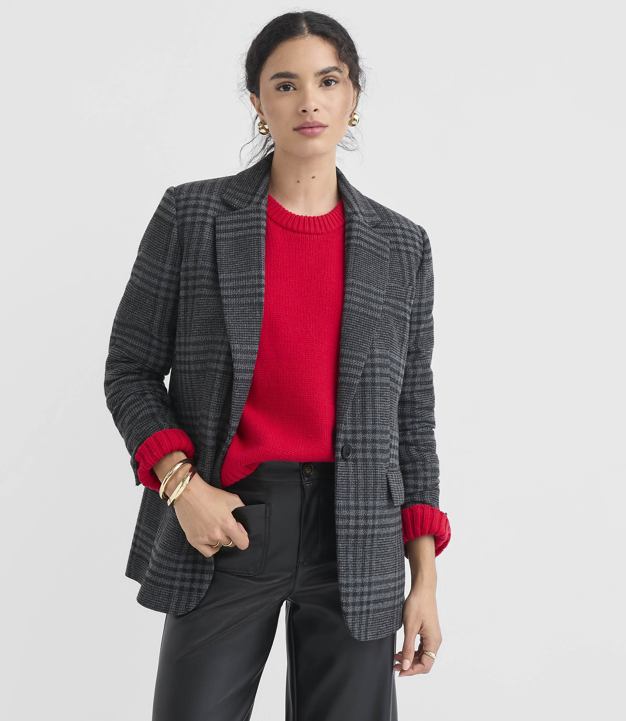 A woman in a red sweater and plaid blazer stands against a plain white background.