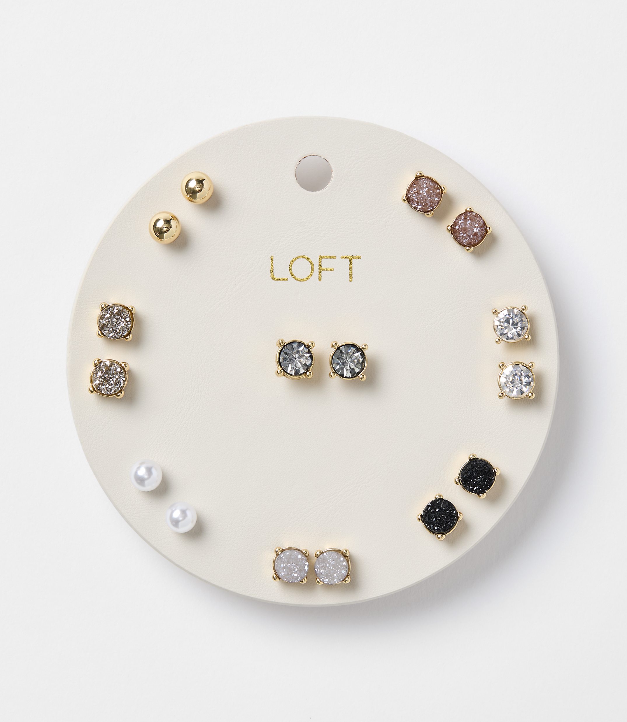 A circular white card displays a collection of assorted stud earrings, including pearls, gold balls, and various gem-encrusted designs, against a plain white background.