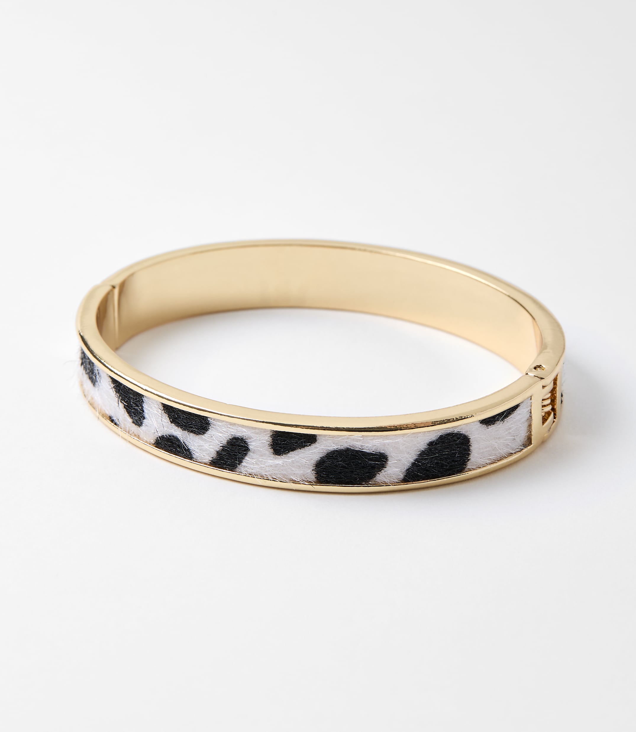 A gold bangle bracelet with a cow print fuzzy inlay rests on a plain white background.