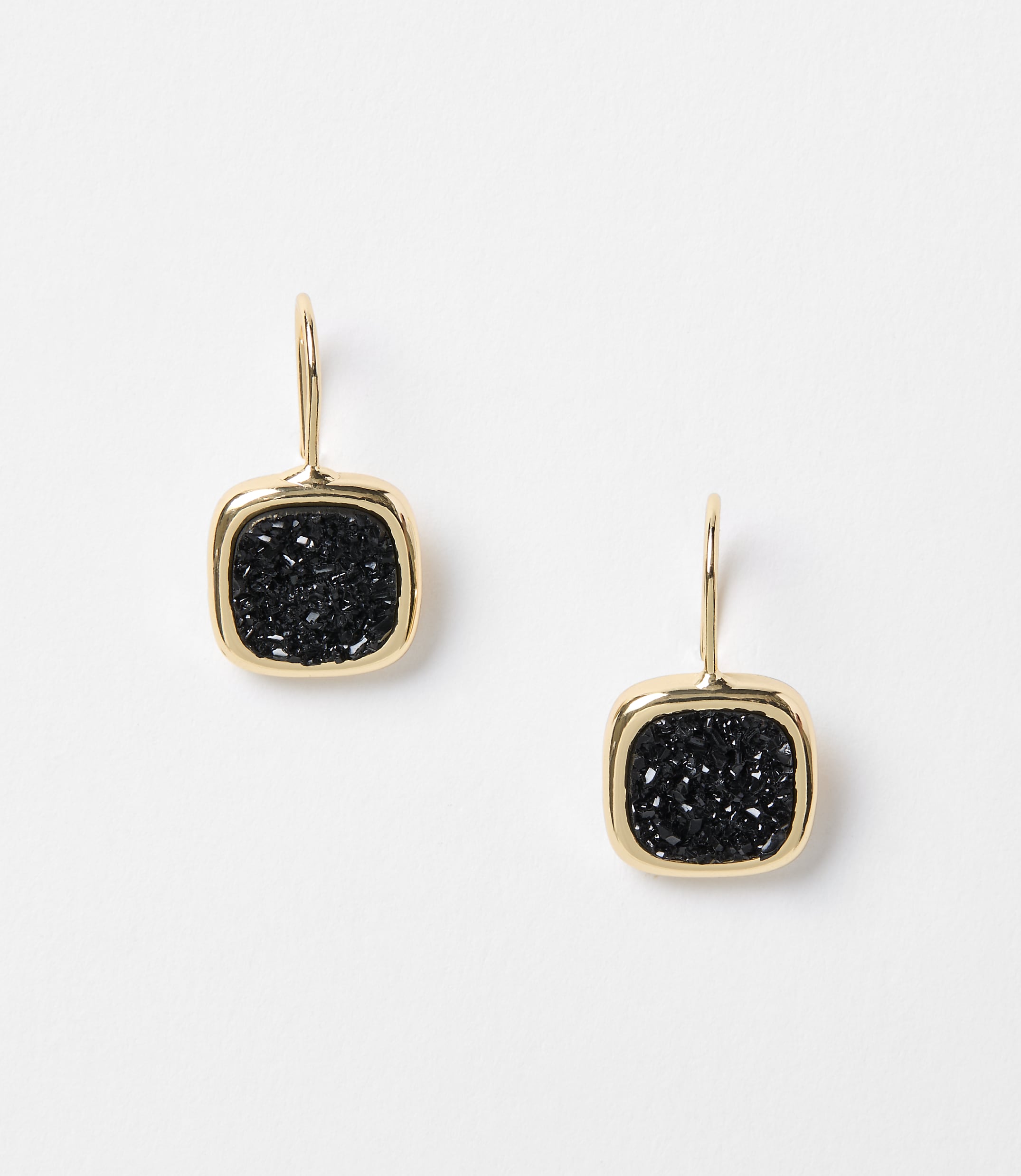 A pair of gold-framed, square black druzy earrings hang against a plain white background.