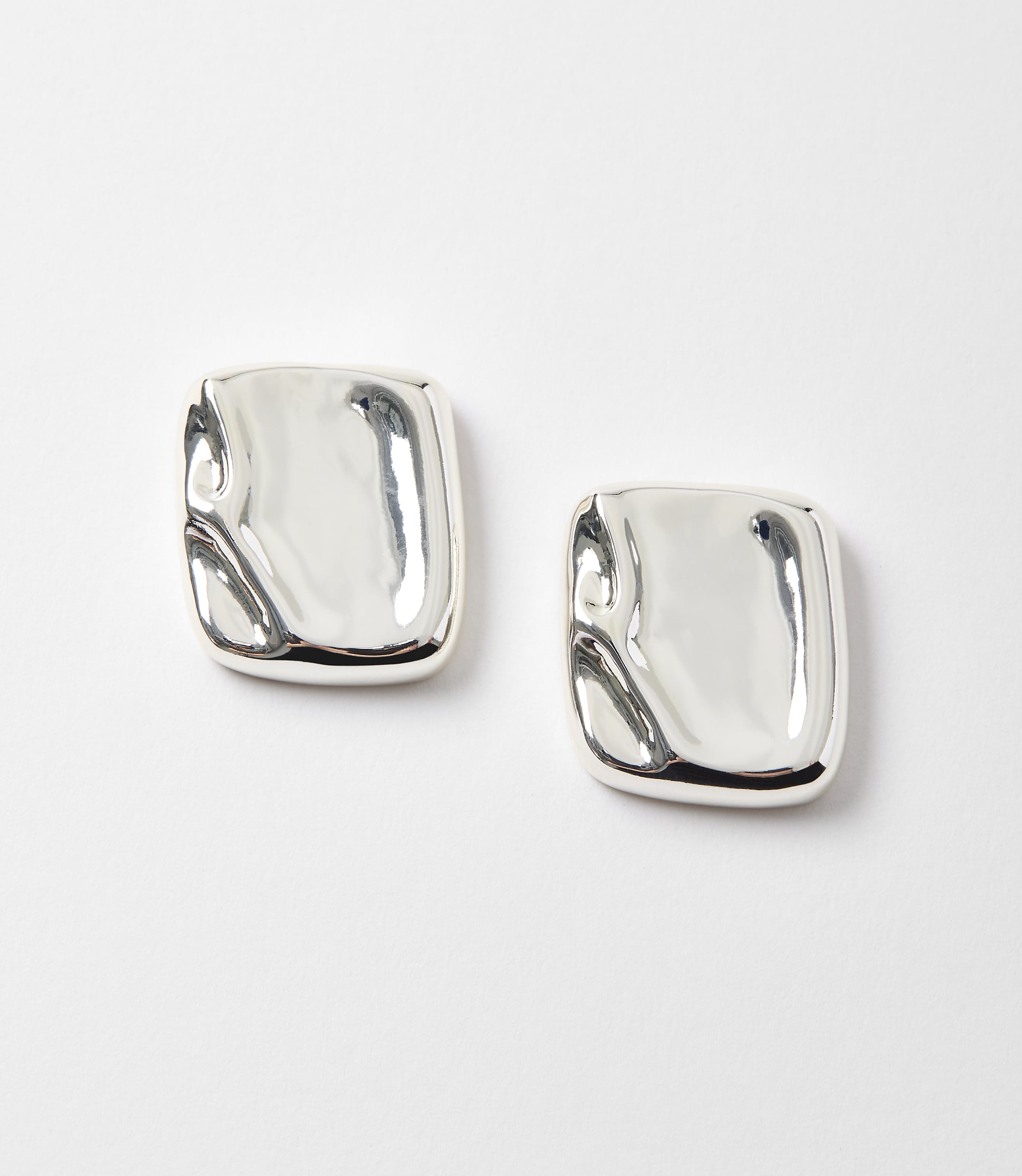 Two abstract, silver square earrings with a molten appearance rest on a plain white background.
