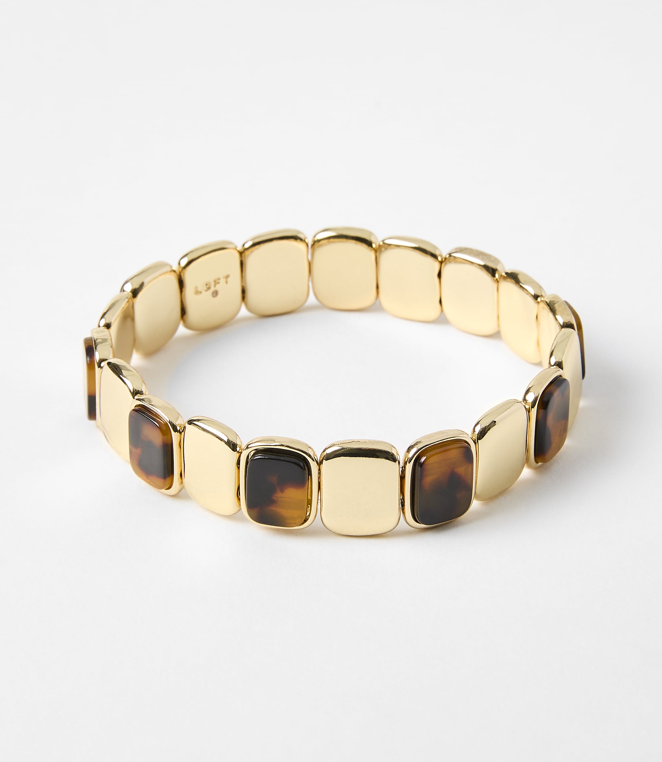 A gold bracelet with square tortoise shell accents rests on a plain white background.