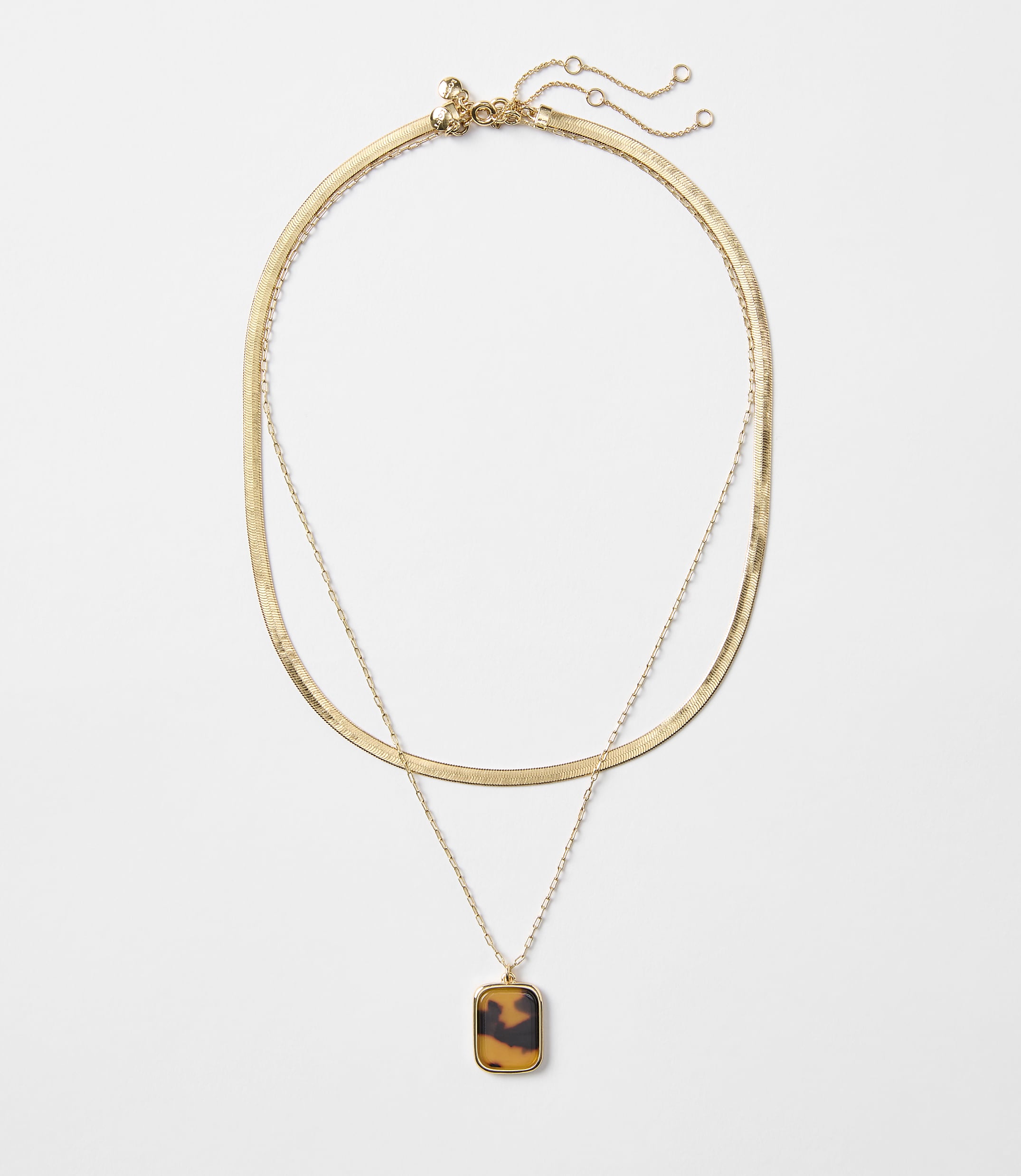 A layered gold necklace with a tortoise shell pendant hangs against a plain white background.
