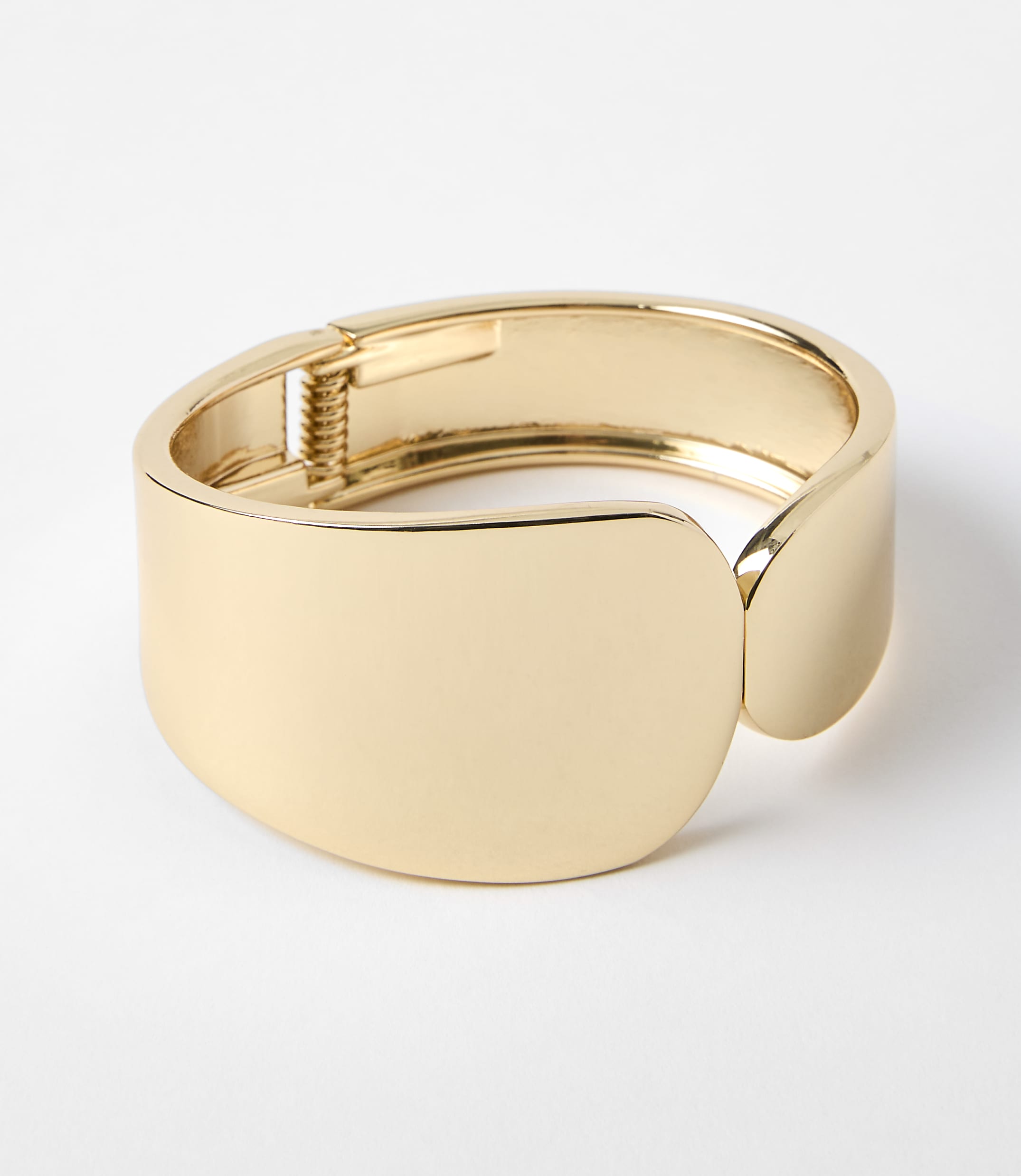 A polished gold cuff bracelet with a hinge closure rests on a plain white background.