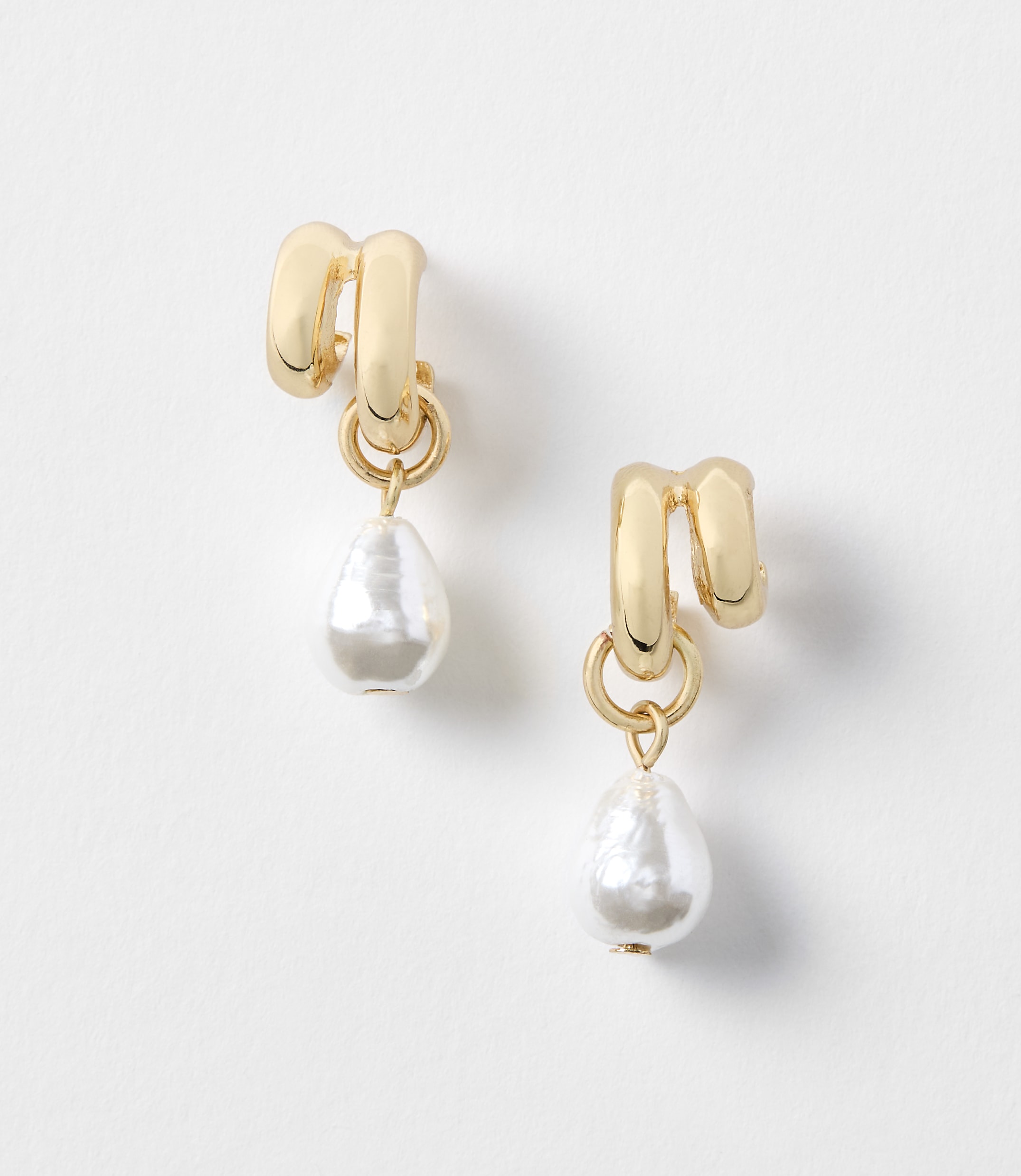 A pair of gold earrings with pearl drops hang against a plain white background.