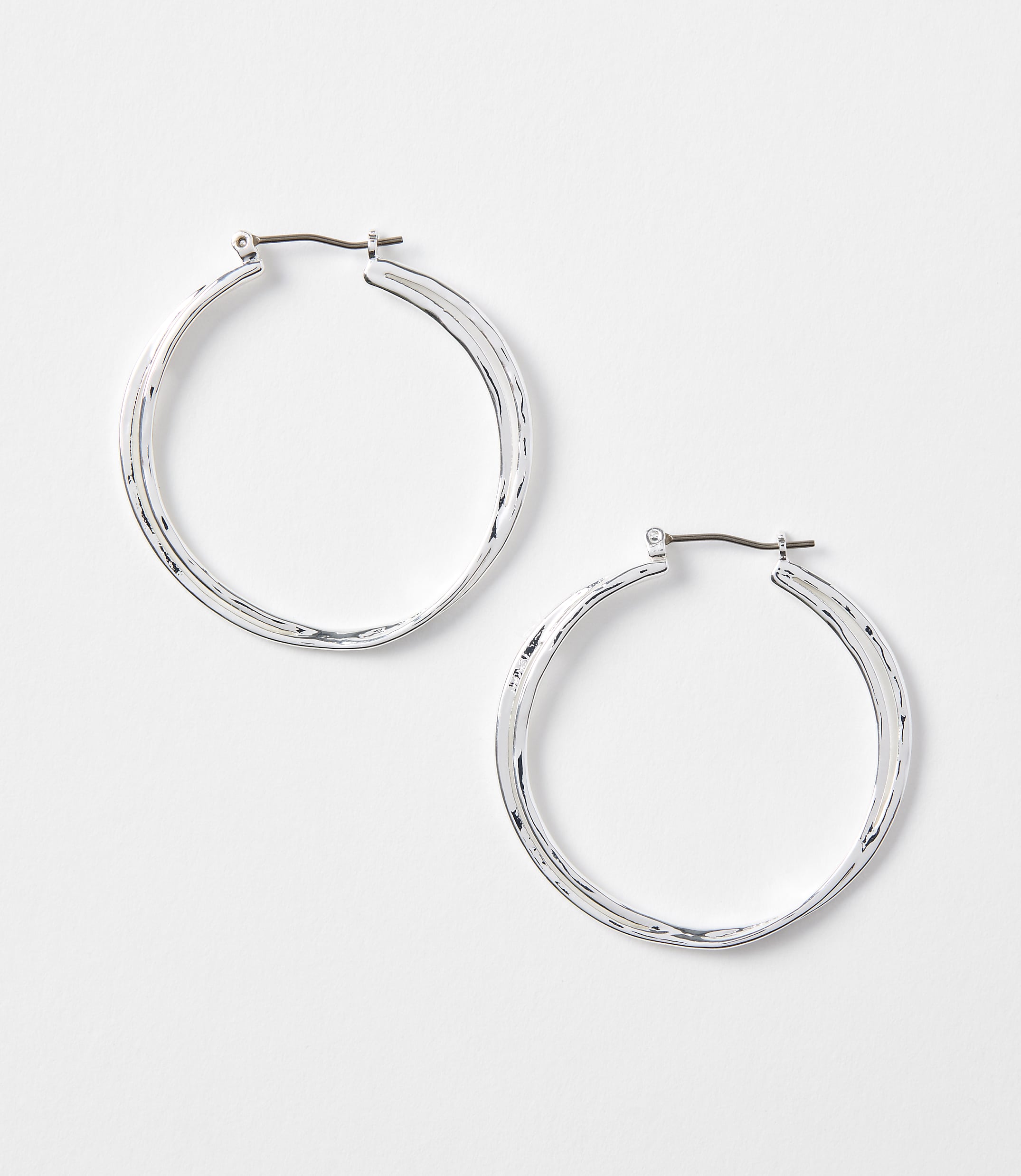 Two silver hoop earrings with textured surfaces rest on a plain white background.