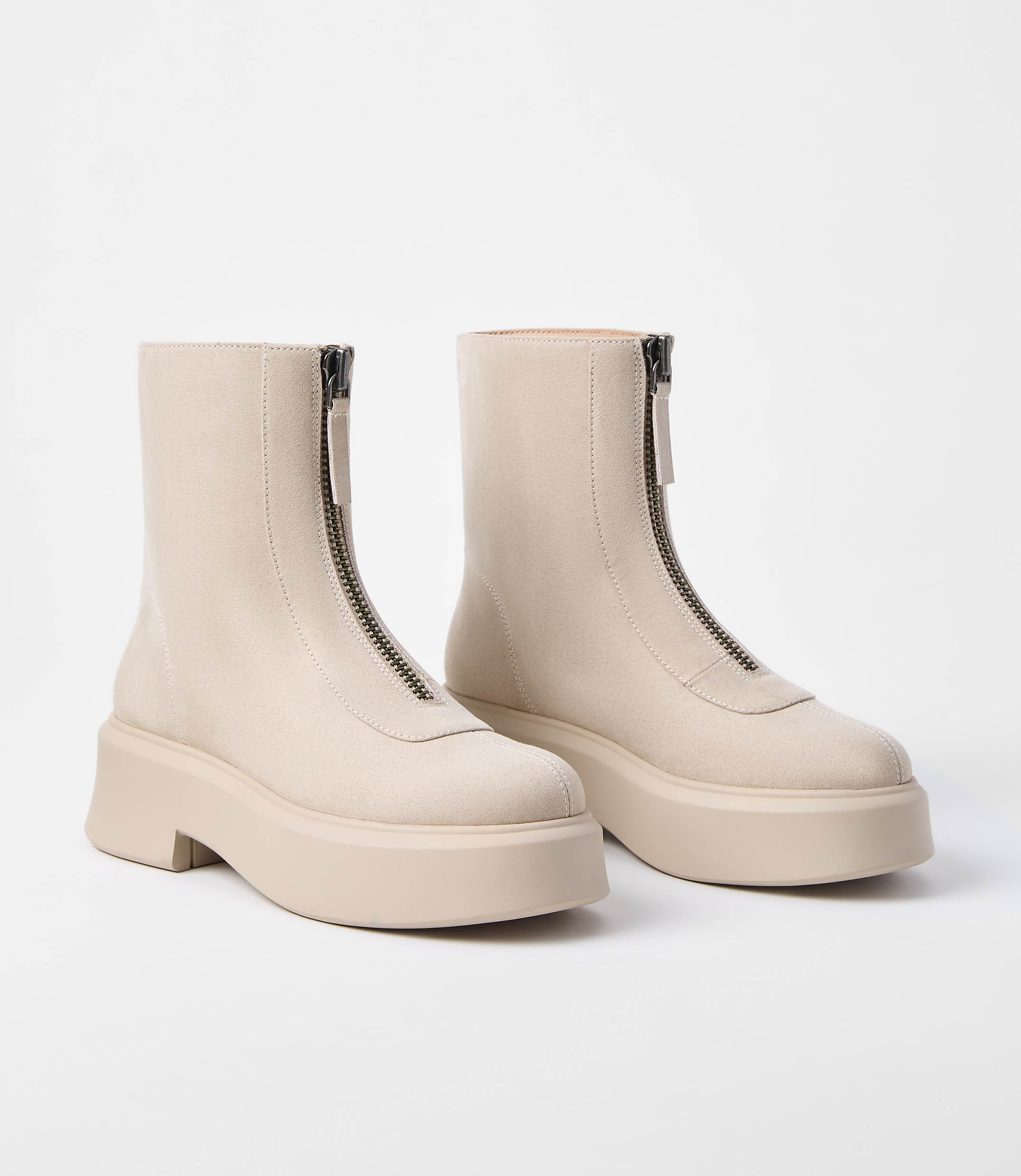 A pair of cream-colored ankle boots with front zippers and thick soles are displayed against a plain white background.