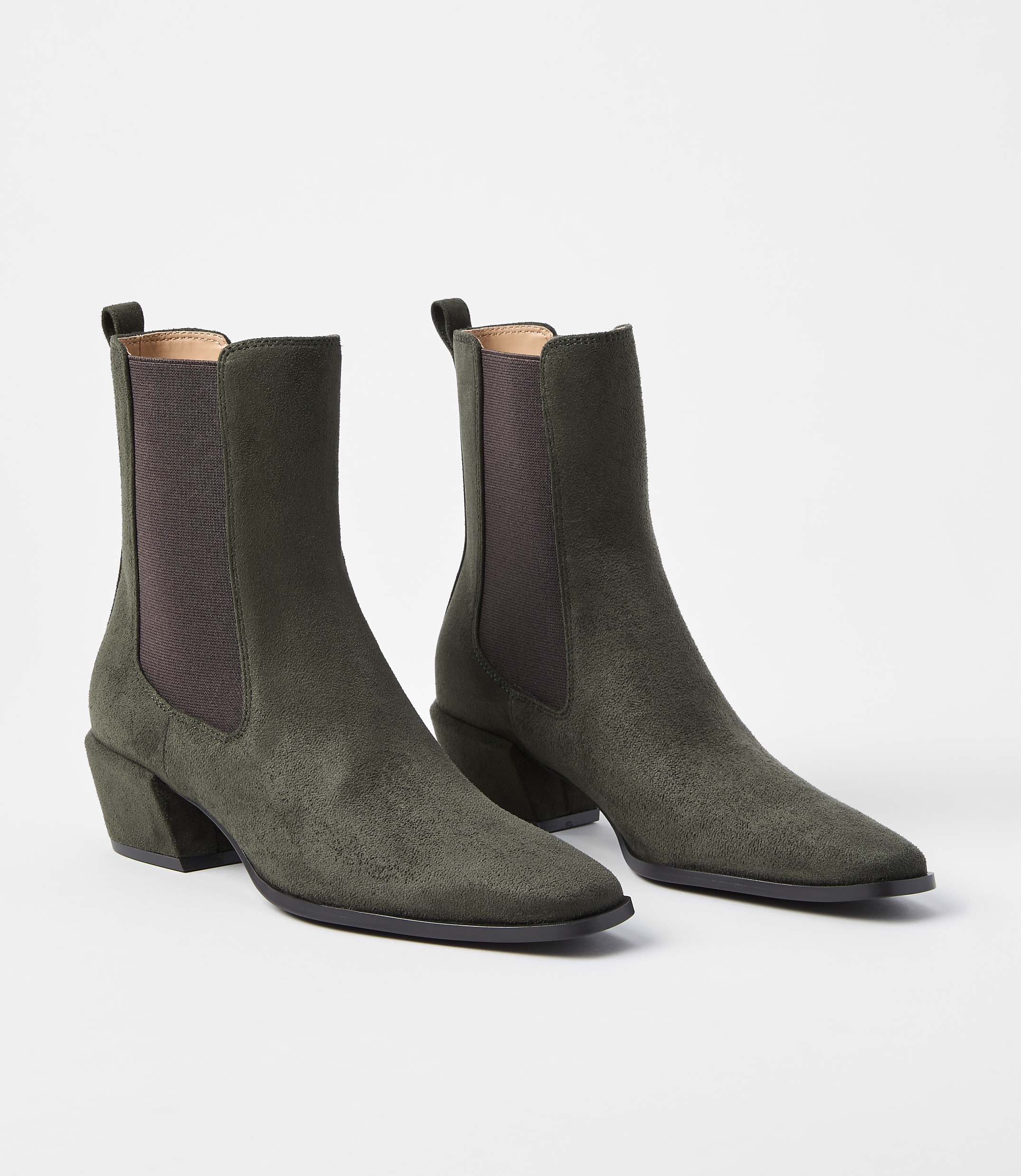 A pair of olive green suede Chelsea boots with block heels rests on a plain white background.