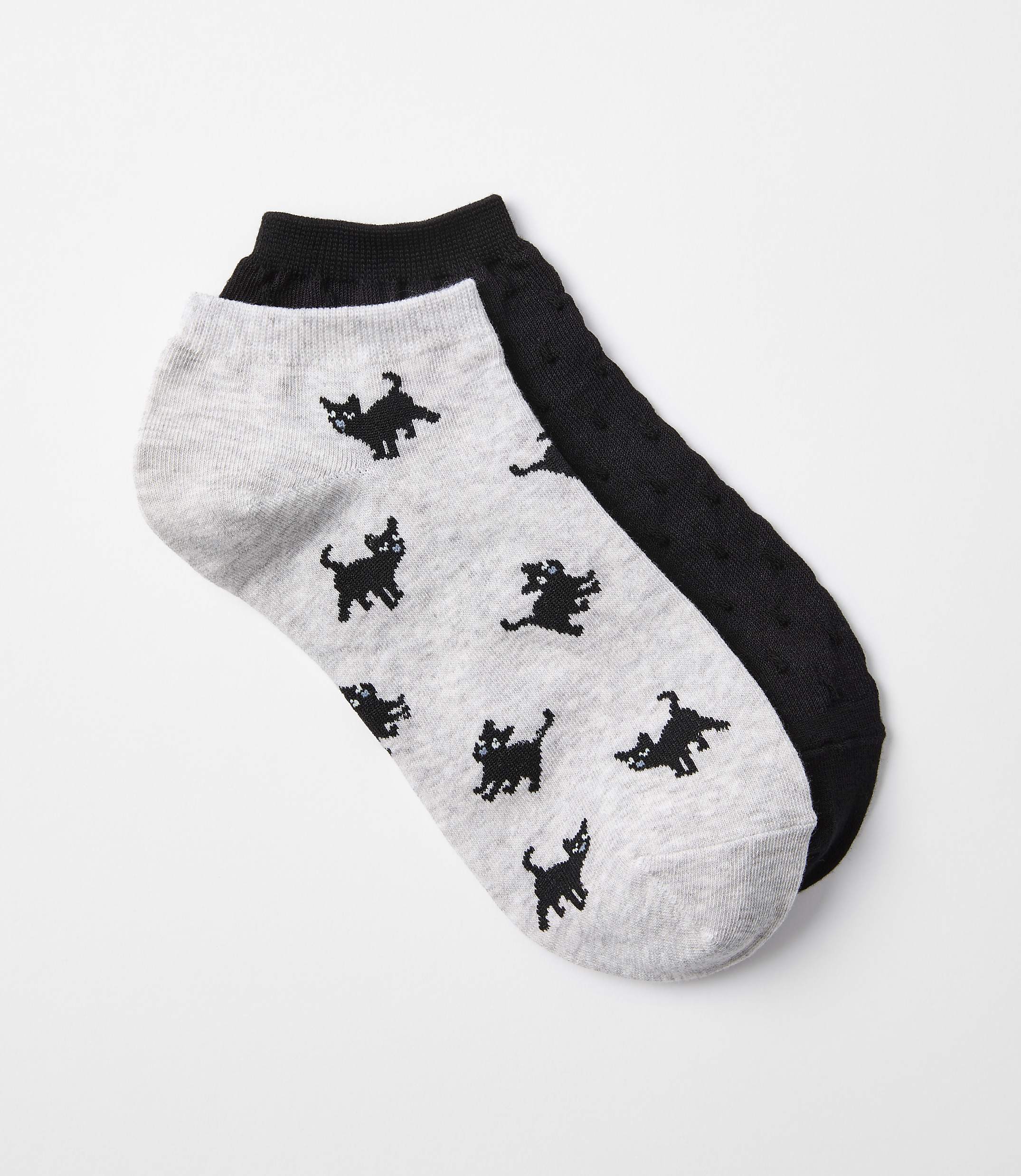 A pair of ankle socks, one light gray with black cat patterns and the other black with a textured pattern, lie on a white background.