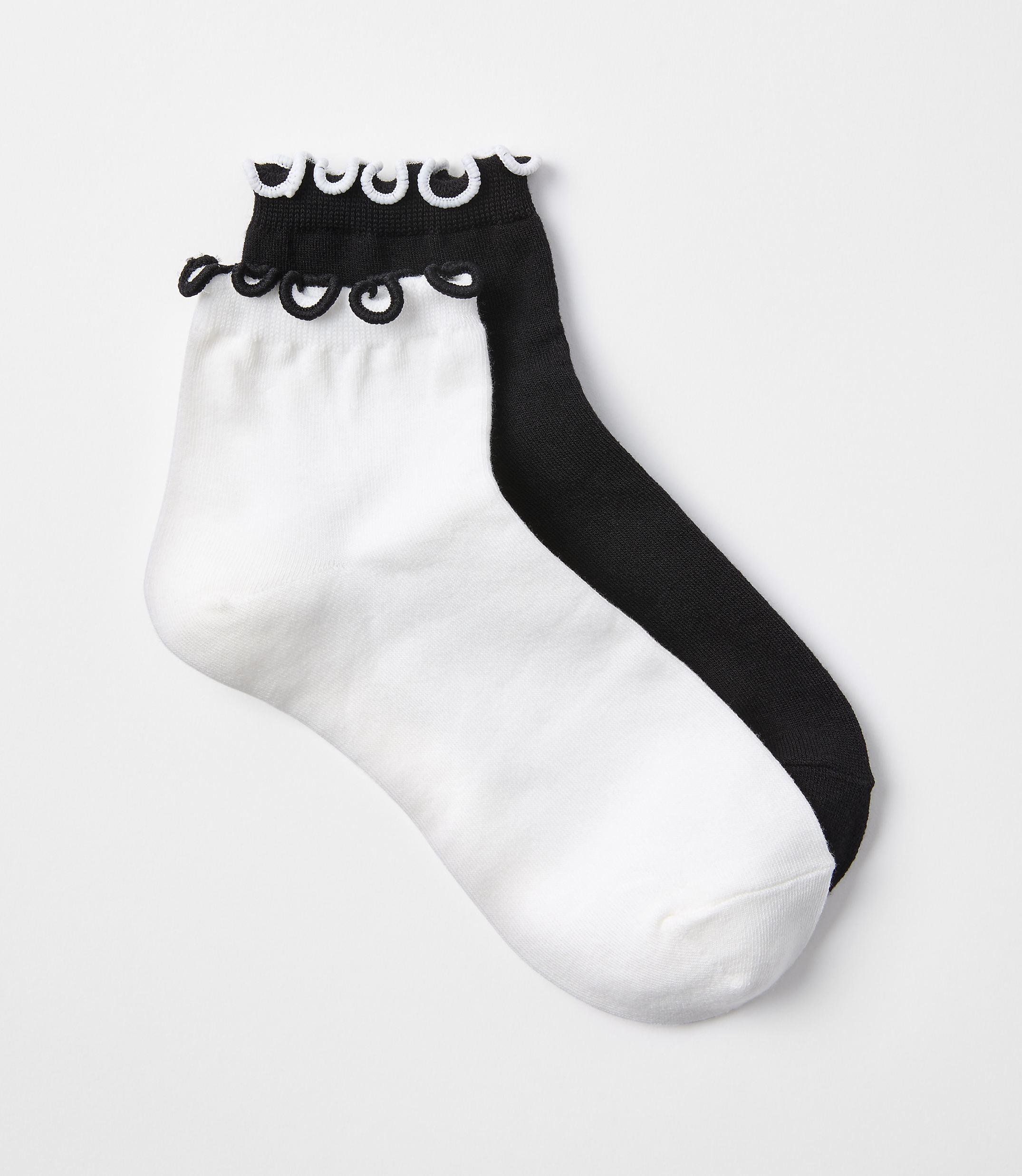 A pair of white and black ankle socks with ruffled cuffs are laid out on a plain white background.
