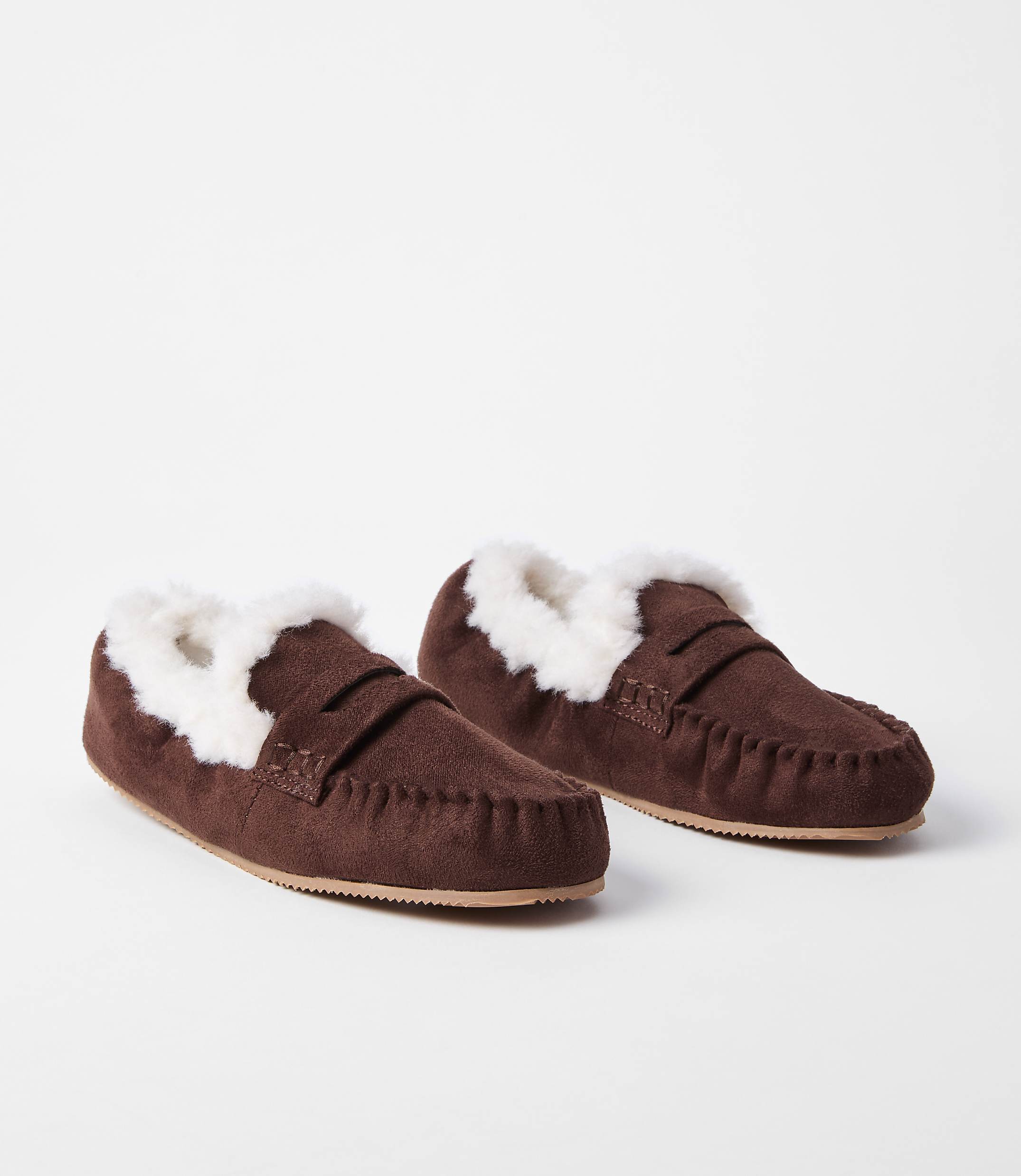A pair of brown suede moccasin slippers with white faux fur lining rests on a plain white background.