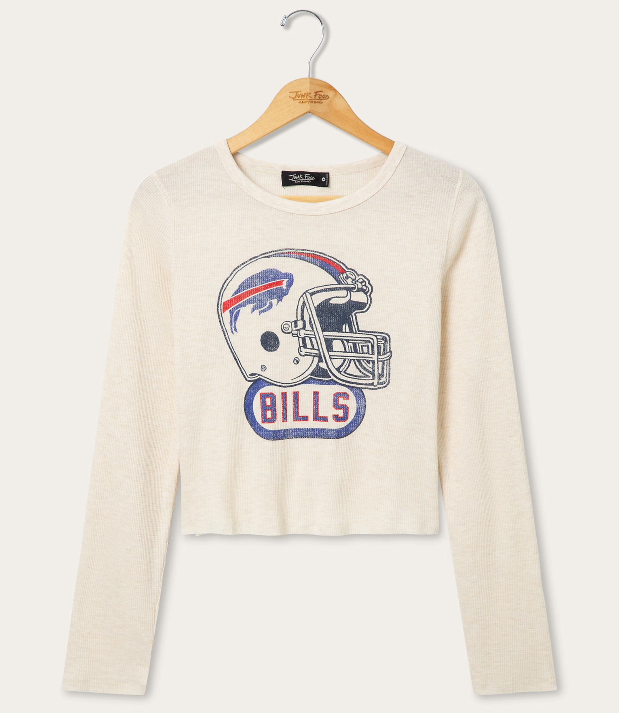 A cream-colored long-sleeved shirt with a vintage Buffalo Bills helmet graphic is displayed on a wooden hanger against a white background.