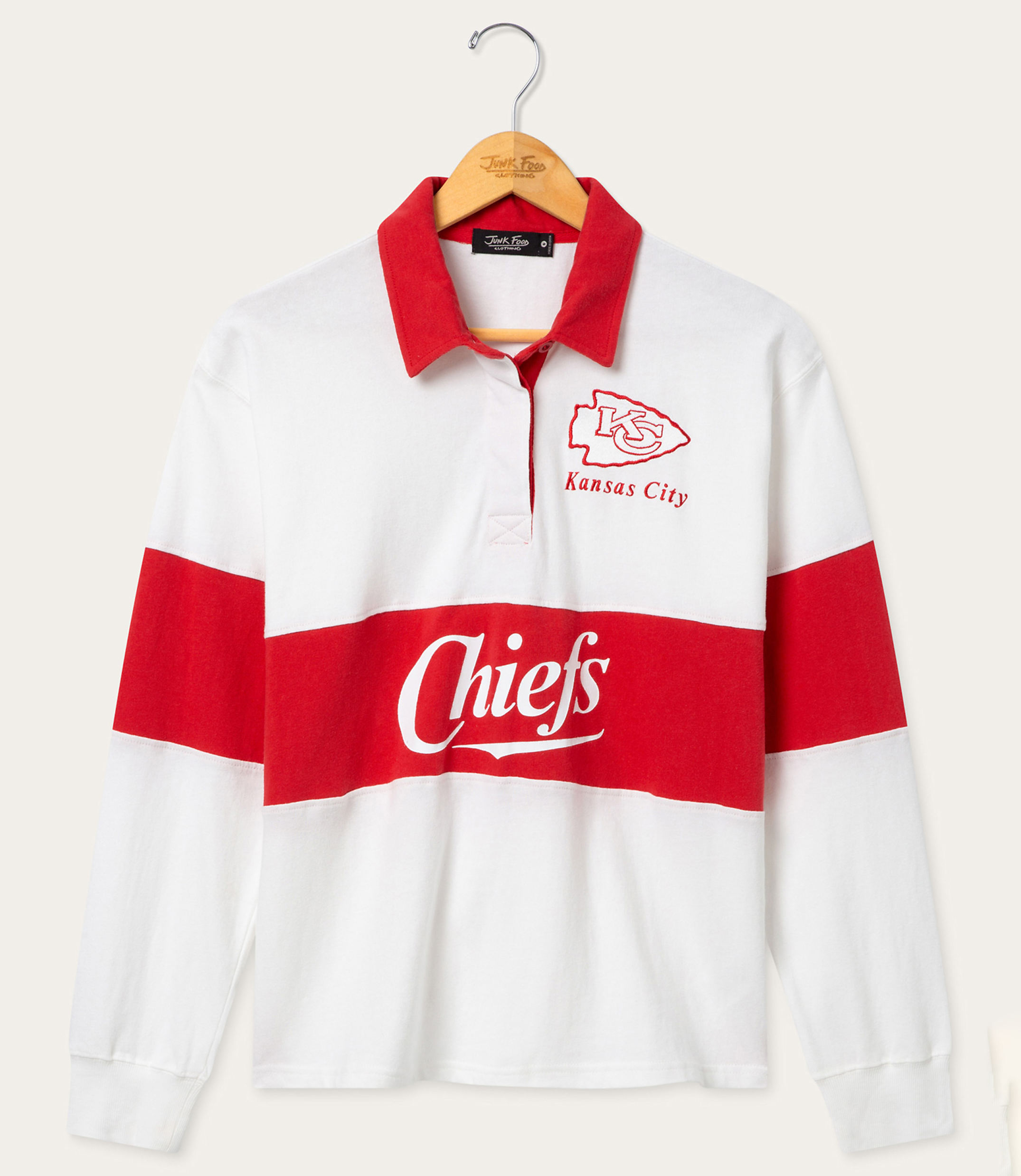 A white and red striped long-sleeved rugby shirt with "Chiefs" and "Kansas City" printed on it hangs on a wooden hanger against a plain white background.