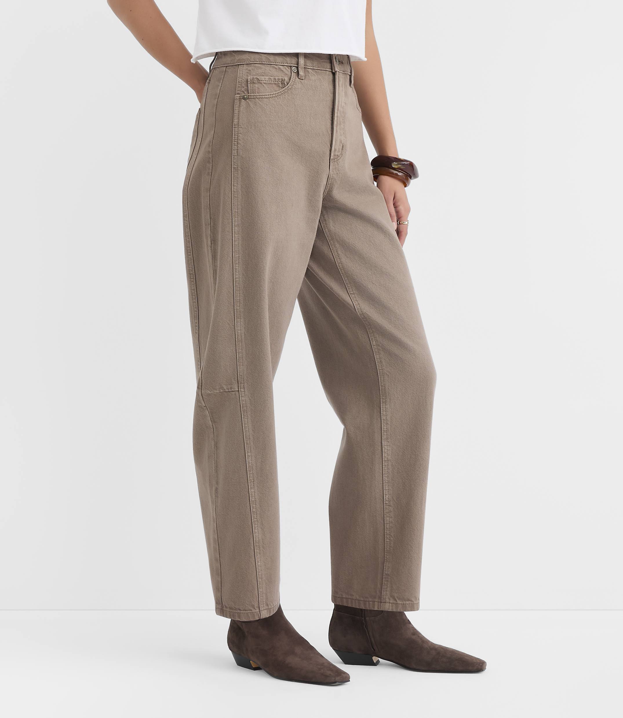 A person stands in loose-fitting, taupe pants and brown ankle boots against a plain white background.