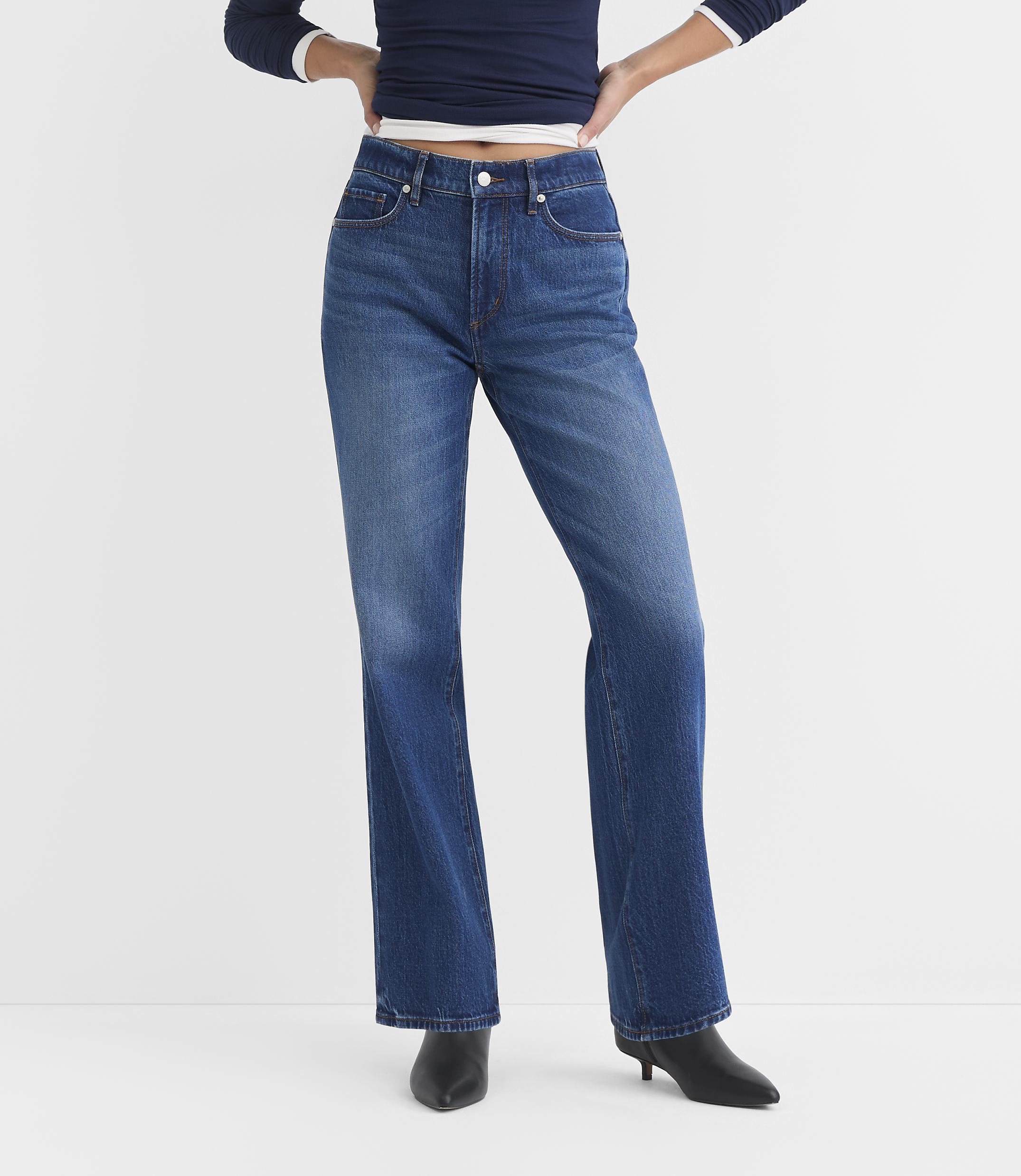 A person wearing blue flared jeans and black heeled boots stands against a plain white background.