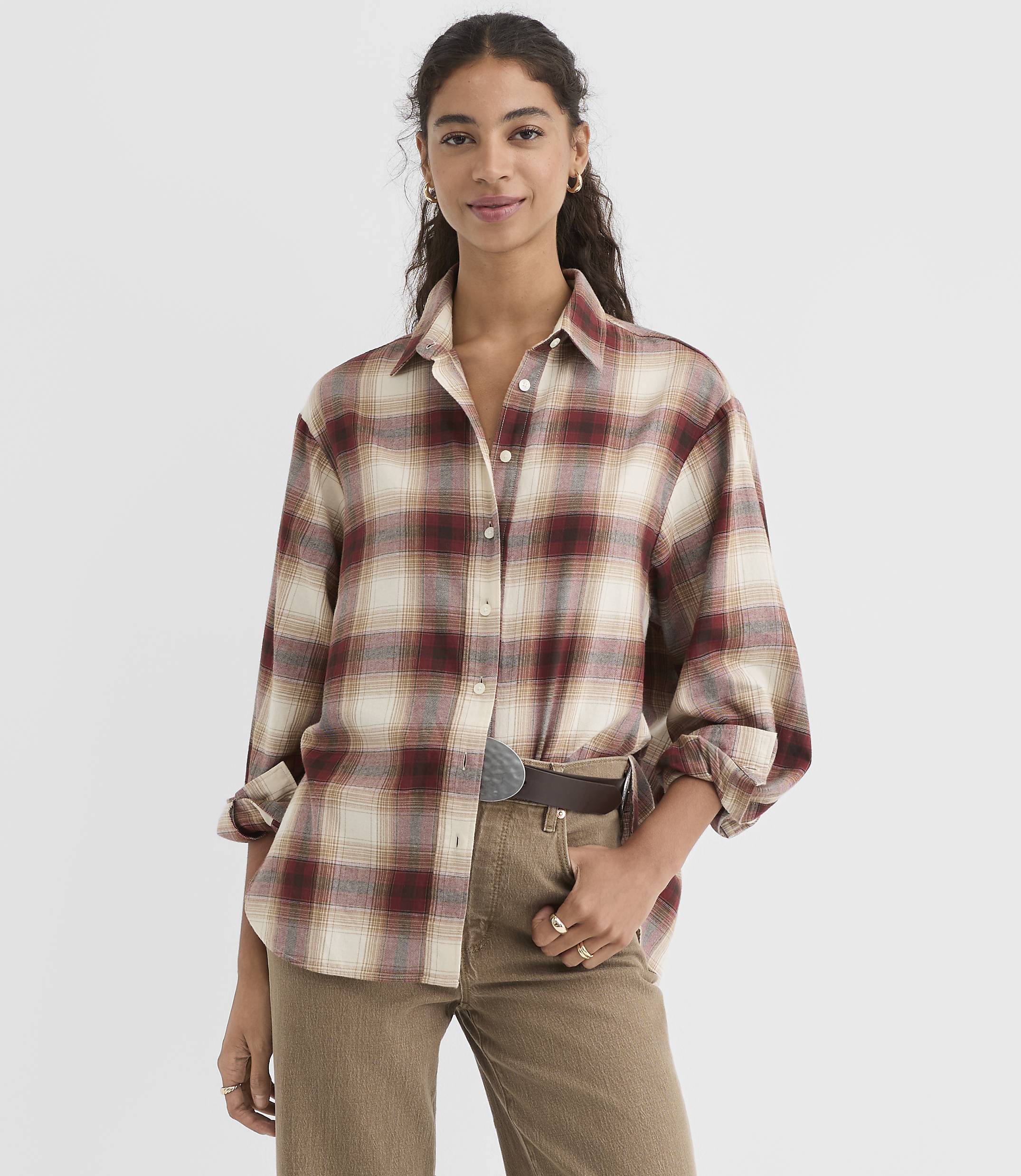 A woman in a plaid shirt and corduroy pants stands against a plain white background.