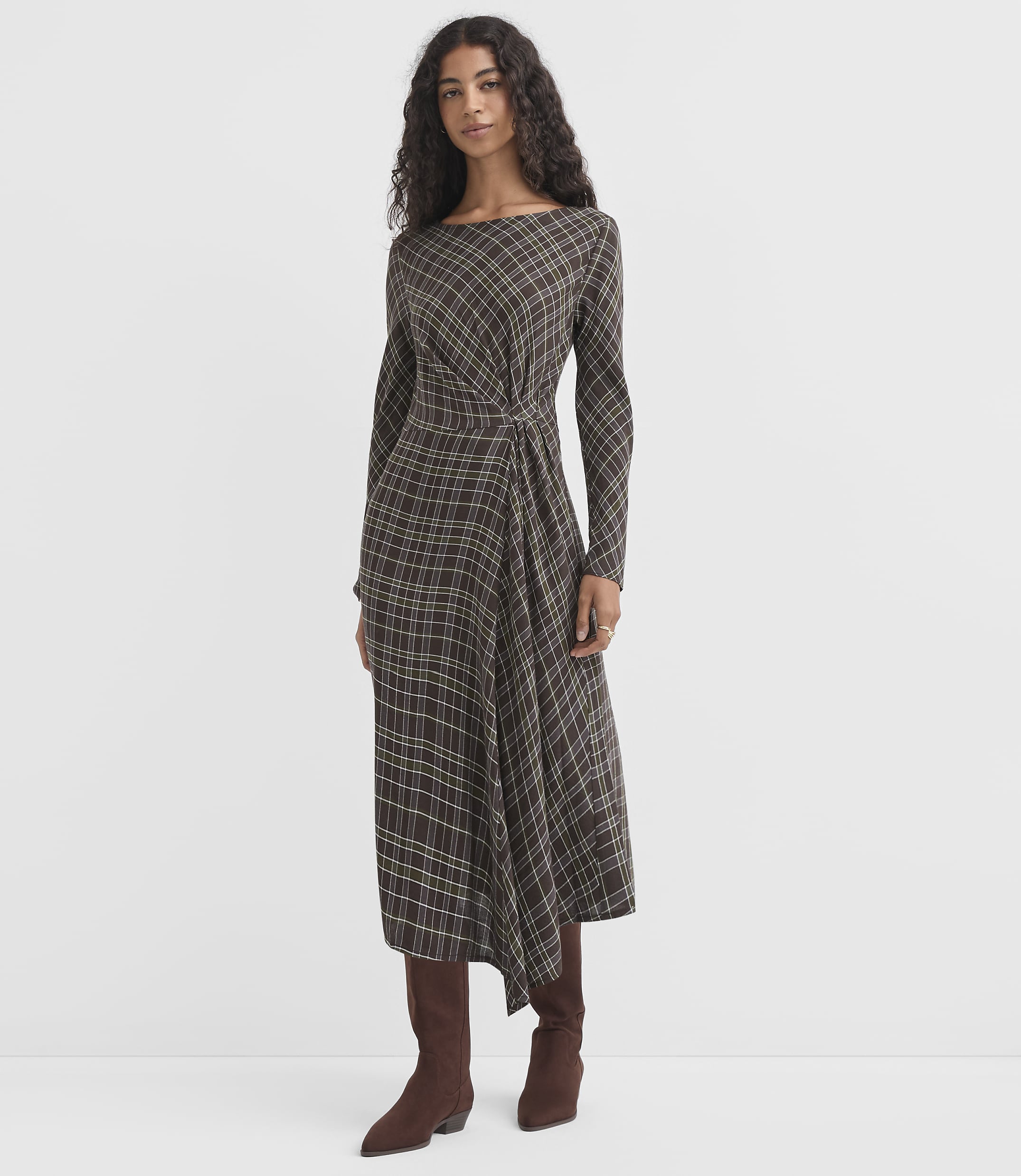 A woman in a plaid dress and boots stands against a plain, light gray background.