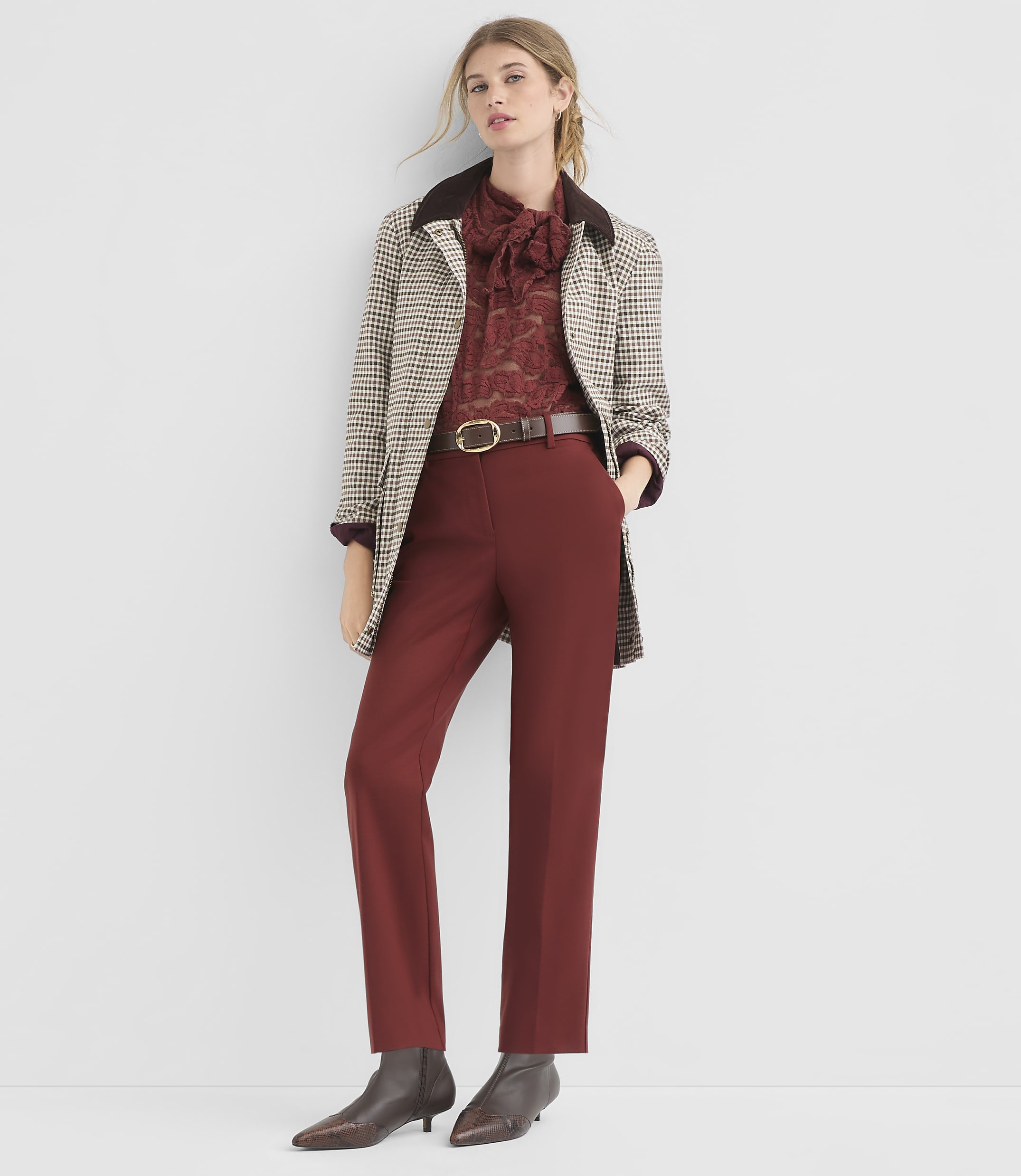 A woman in a patterned jacket and maroon pants stands against a plain white background.