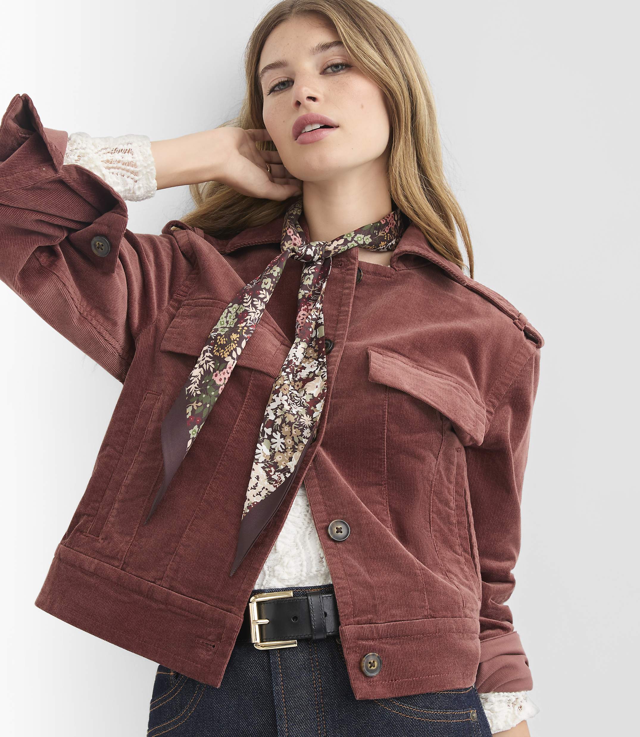 A woman in a rust-colored corduroy jacket and floral scarf poses against a plain white background.